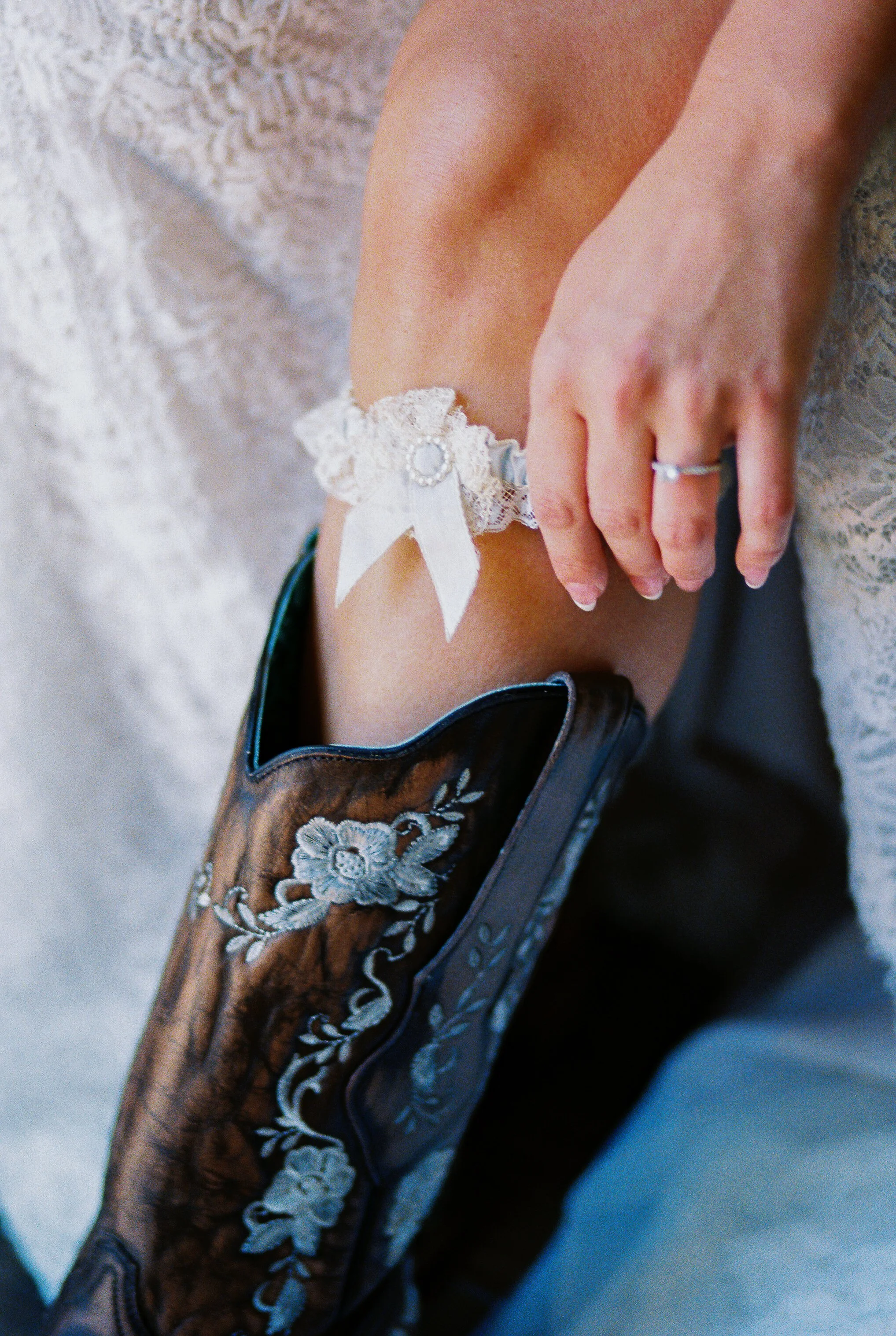 Close-up detail of the bride's lace garter and cowboy boot, with her hand and wedding ring resting on her leg
