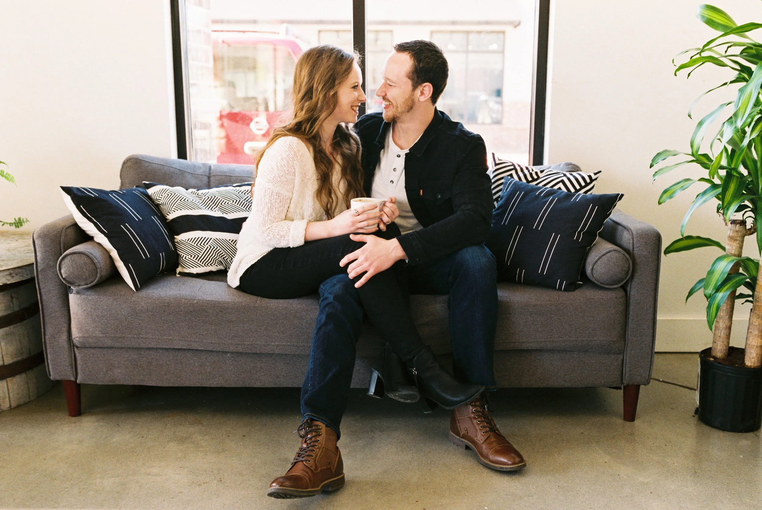 Conner and Maddie laugh together on a couch beside a large potted plant in a Dallas, Georgia coffee shop.