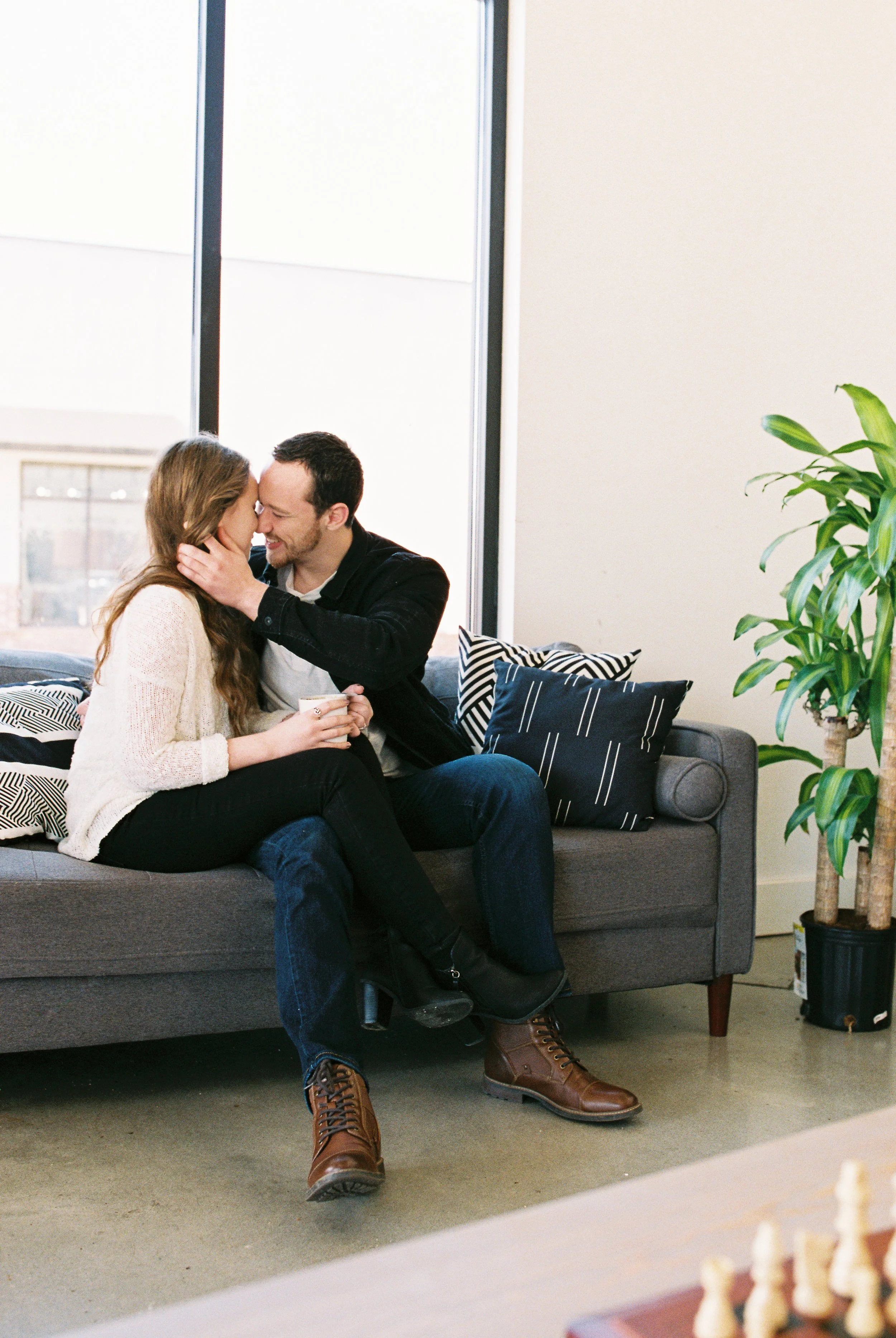 Conner and Maddie kiss on a couch with a chess board in the foreground at a Dallas, Georgia coffee shop.