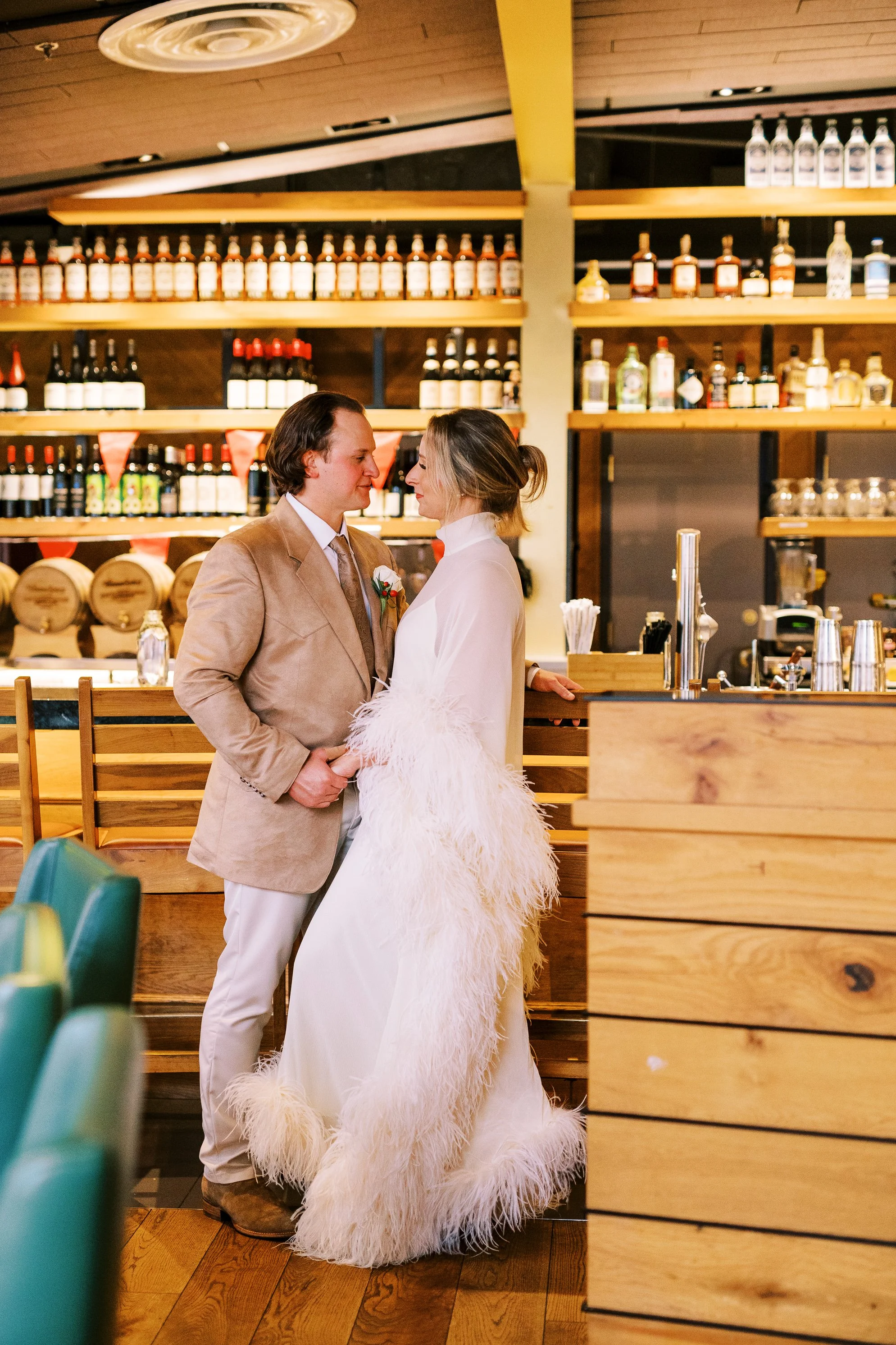 Bride and groom standing together in front of a wooden bar lined with bottles