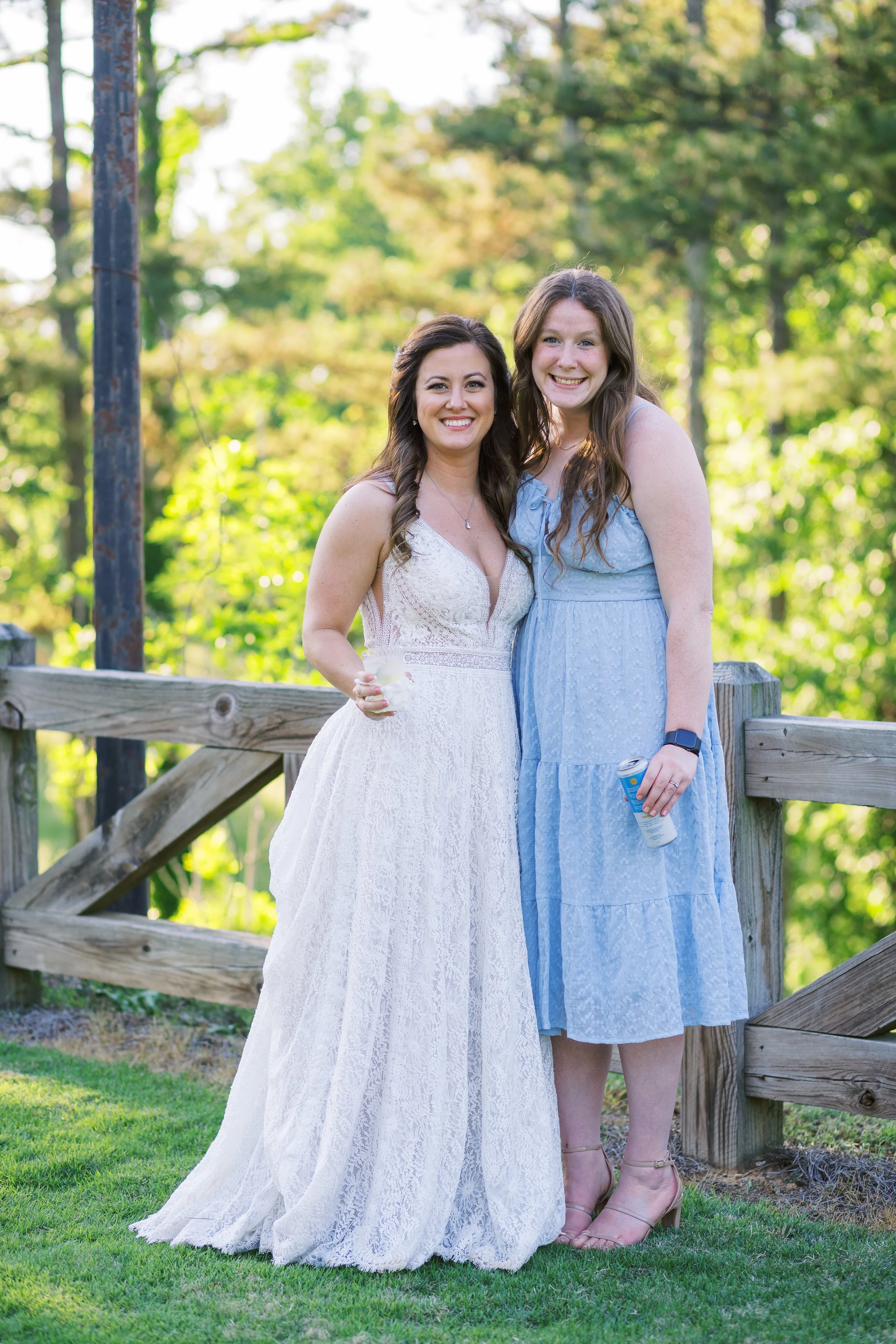 Bride and a bridesmaid in a blue dress posing together on a wooden bridge