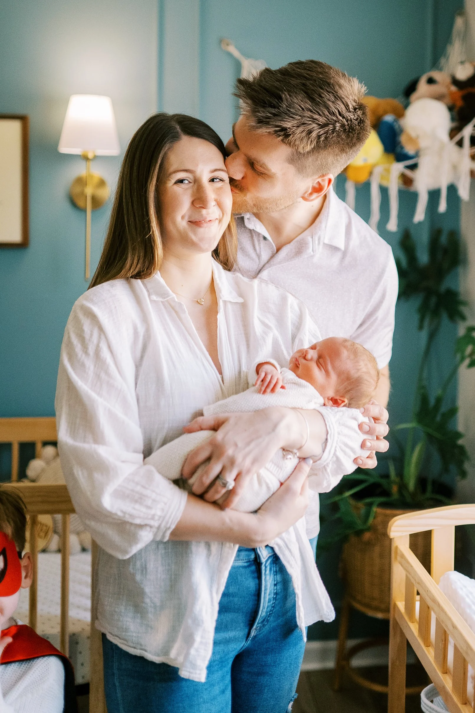 Dad kissing mom's forehead while she holds their newborn baby in the nursery, Roswell, Georgia