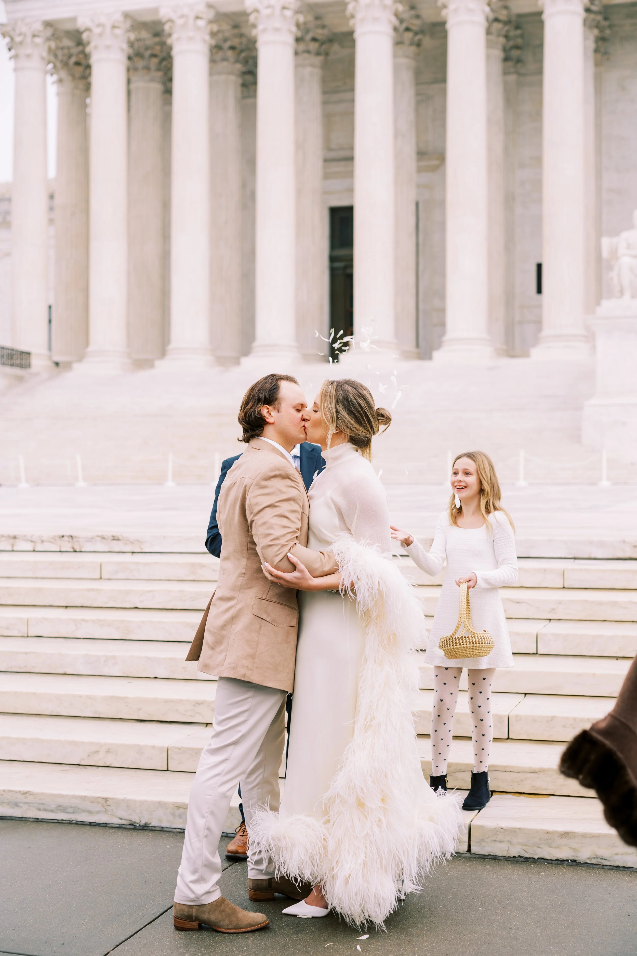 Bride and groom kissing with their flower girl beside a grand columned building