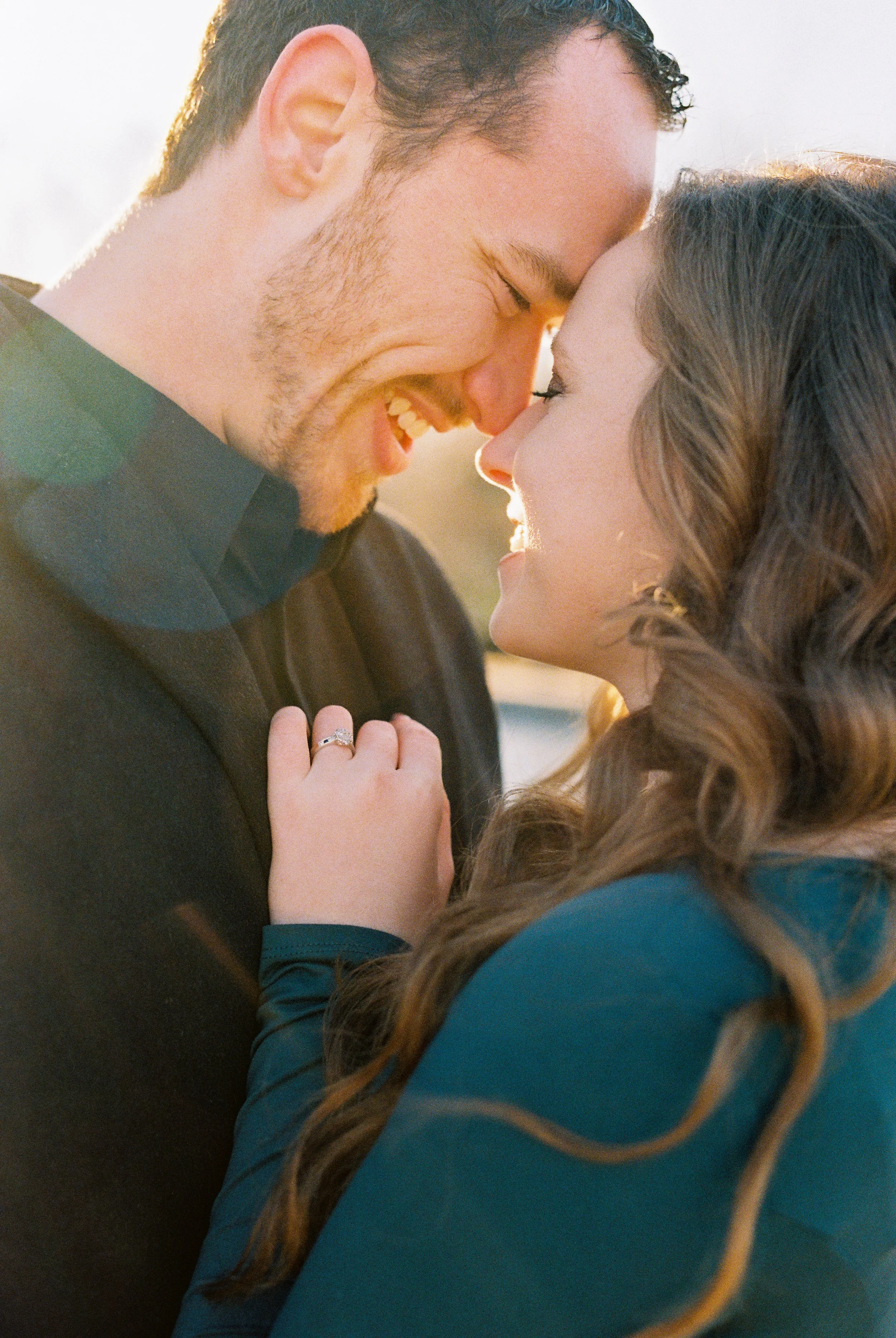 A couple sharing a close, joyful moment with their foreheads touching, smiling, outdoors at sunset.