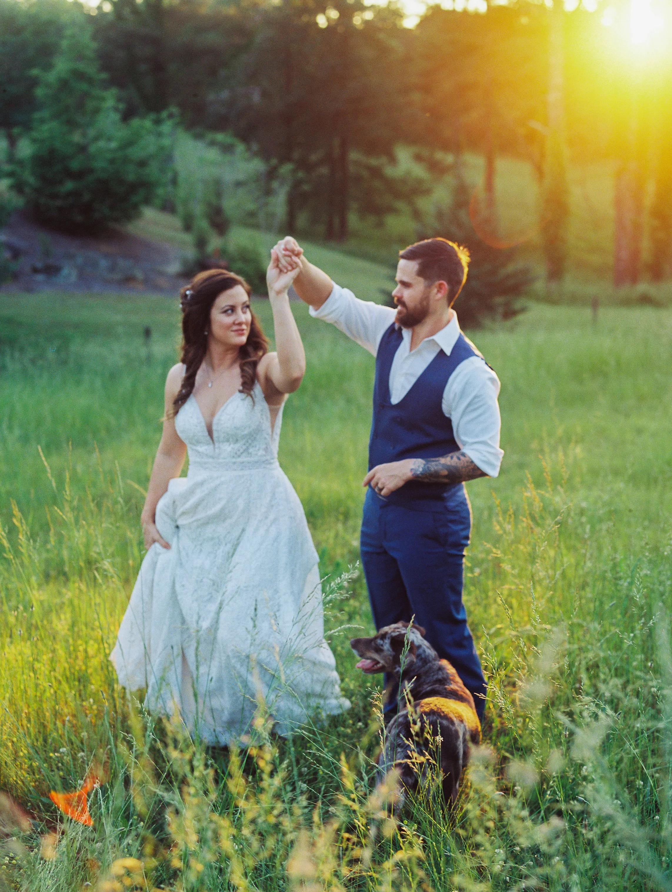 A couple dancing in a grassy field during sunset, with a dog sitting nearby.