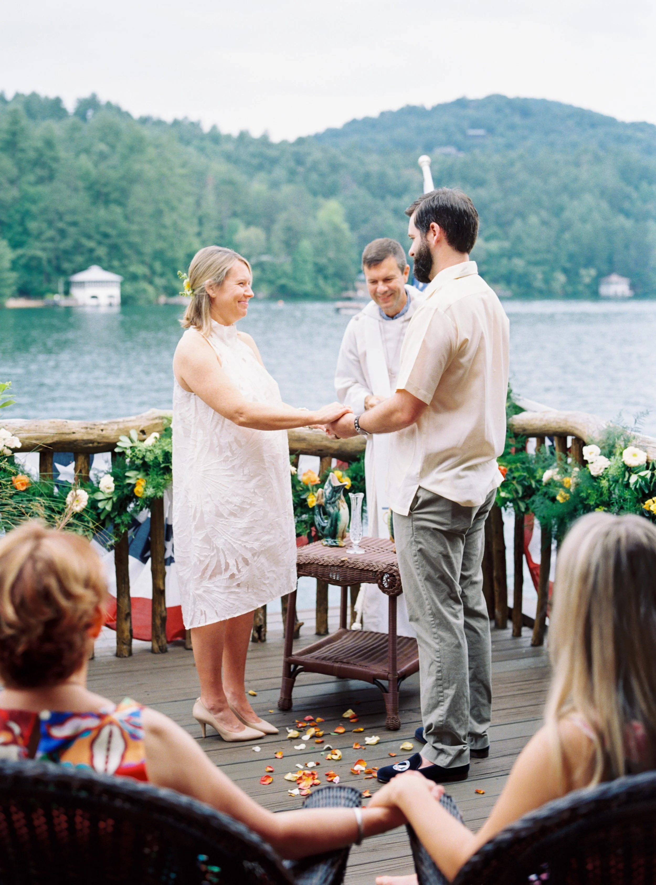 Bride and groom holding hands during their lakeside wedding ceremony with guests seated nearby