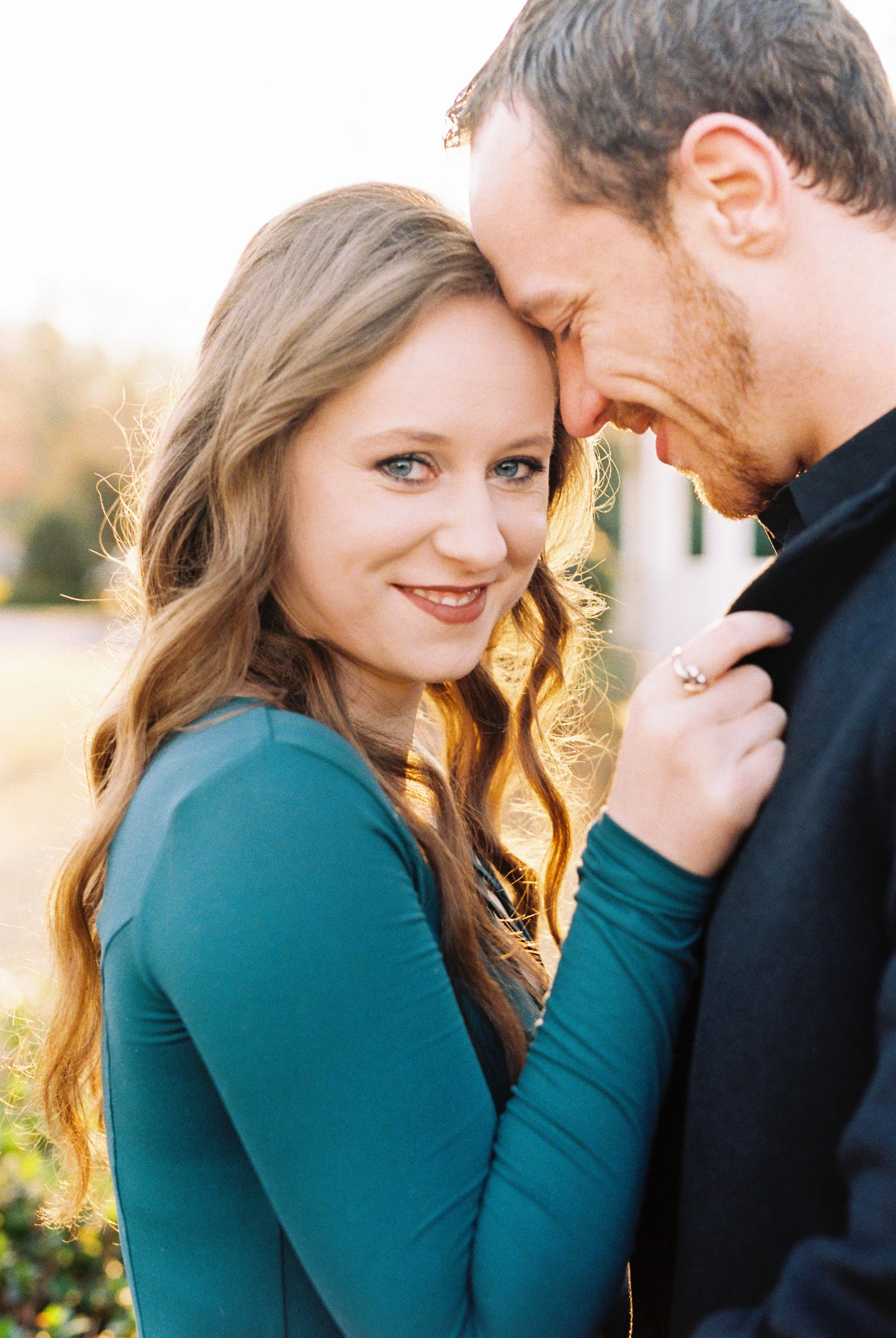 A close-up of Maddie smiling at the camera as Conner laughs beside her, her engagement ring visible, at golden hour in Dallas, Georgia.