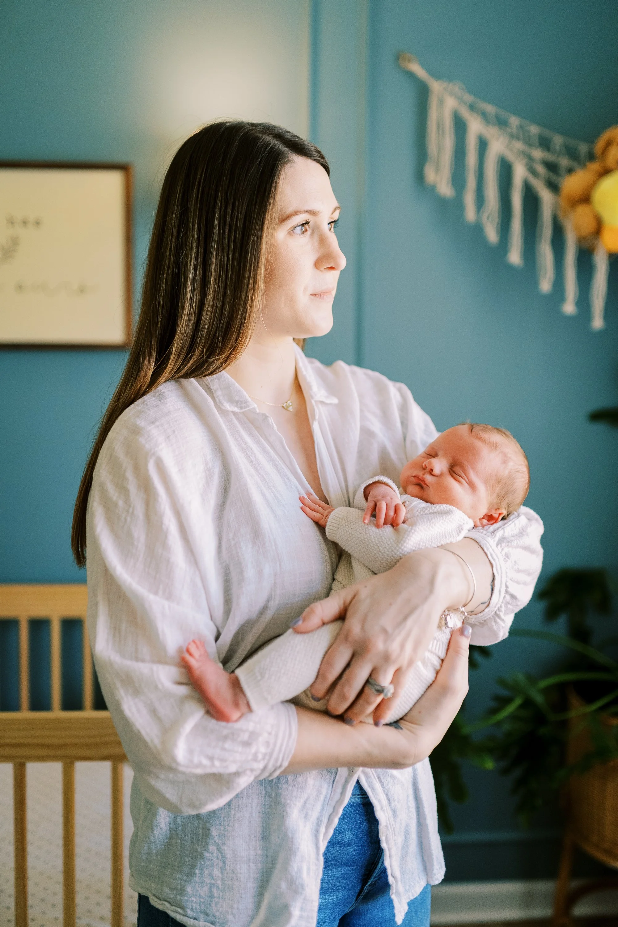 Mother standing beside the crib holding her sleeping newborn in the nursery, Roswell, Georgia