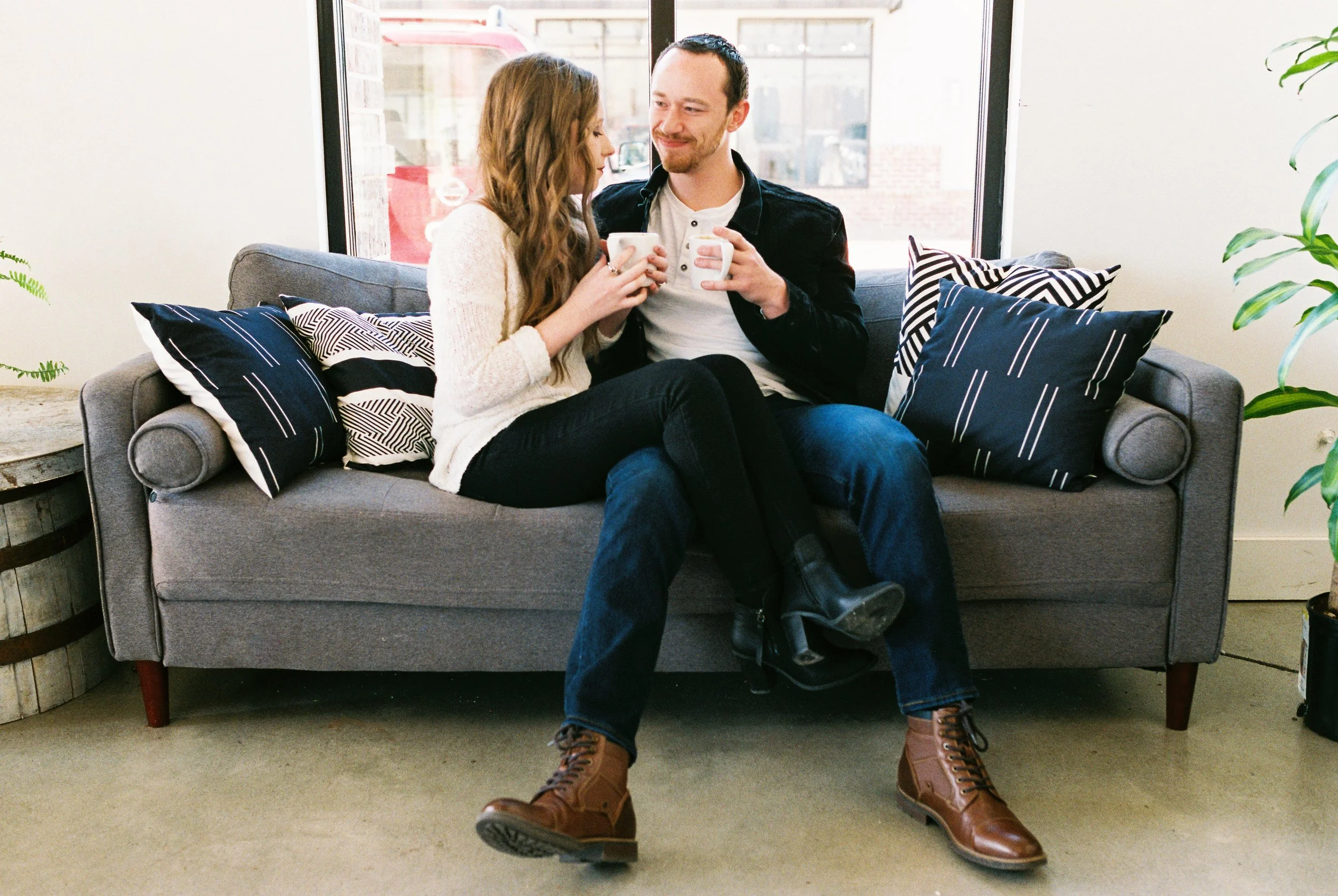 Conner and Maddie sit on a couch holding coffee mugs together in a Dallas, Georgia coffee shop.