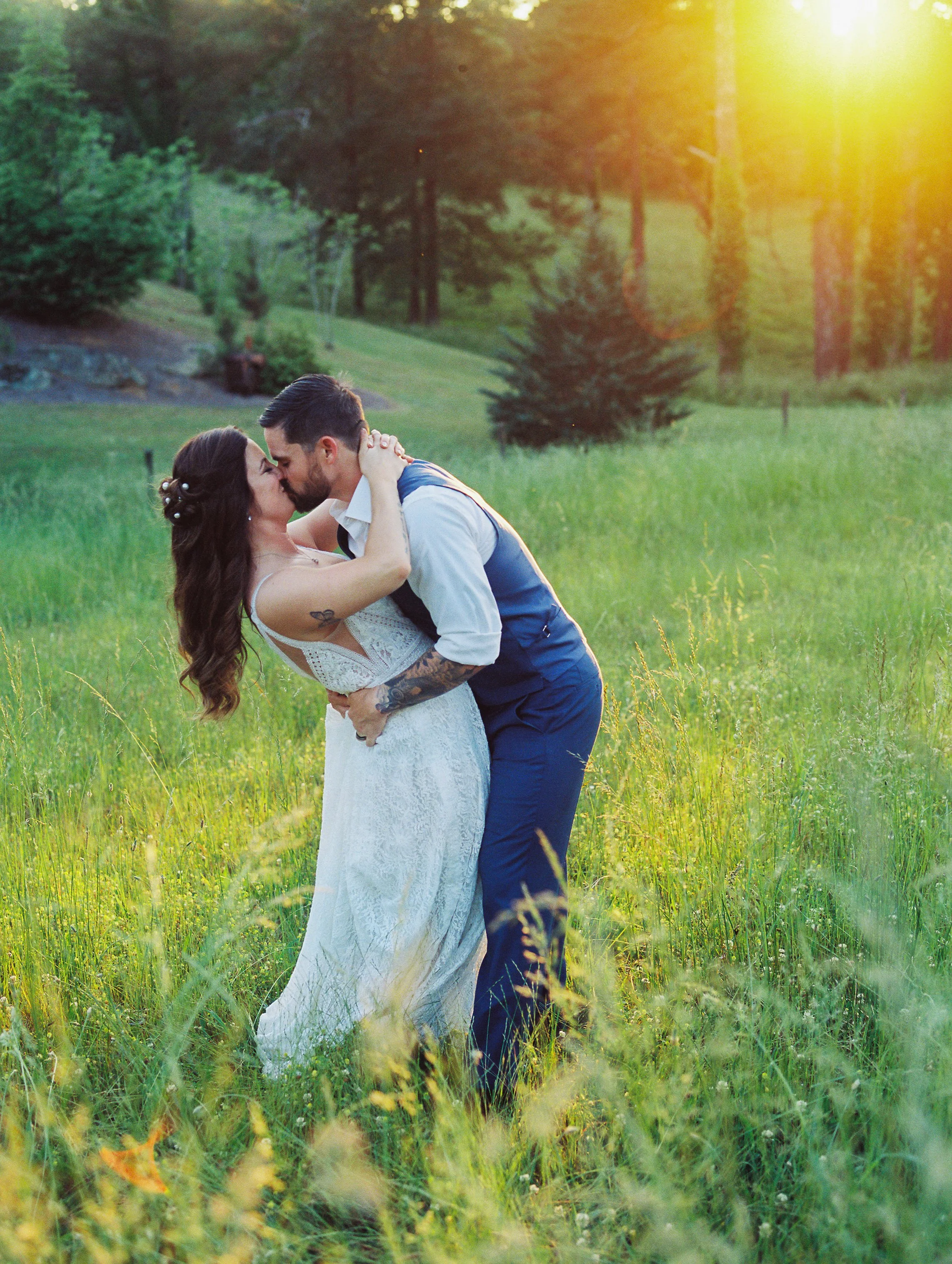 Groom dipping and kissing the bride in a sunlit golden field surrounded by tall grass