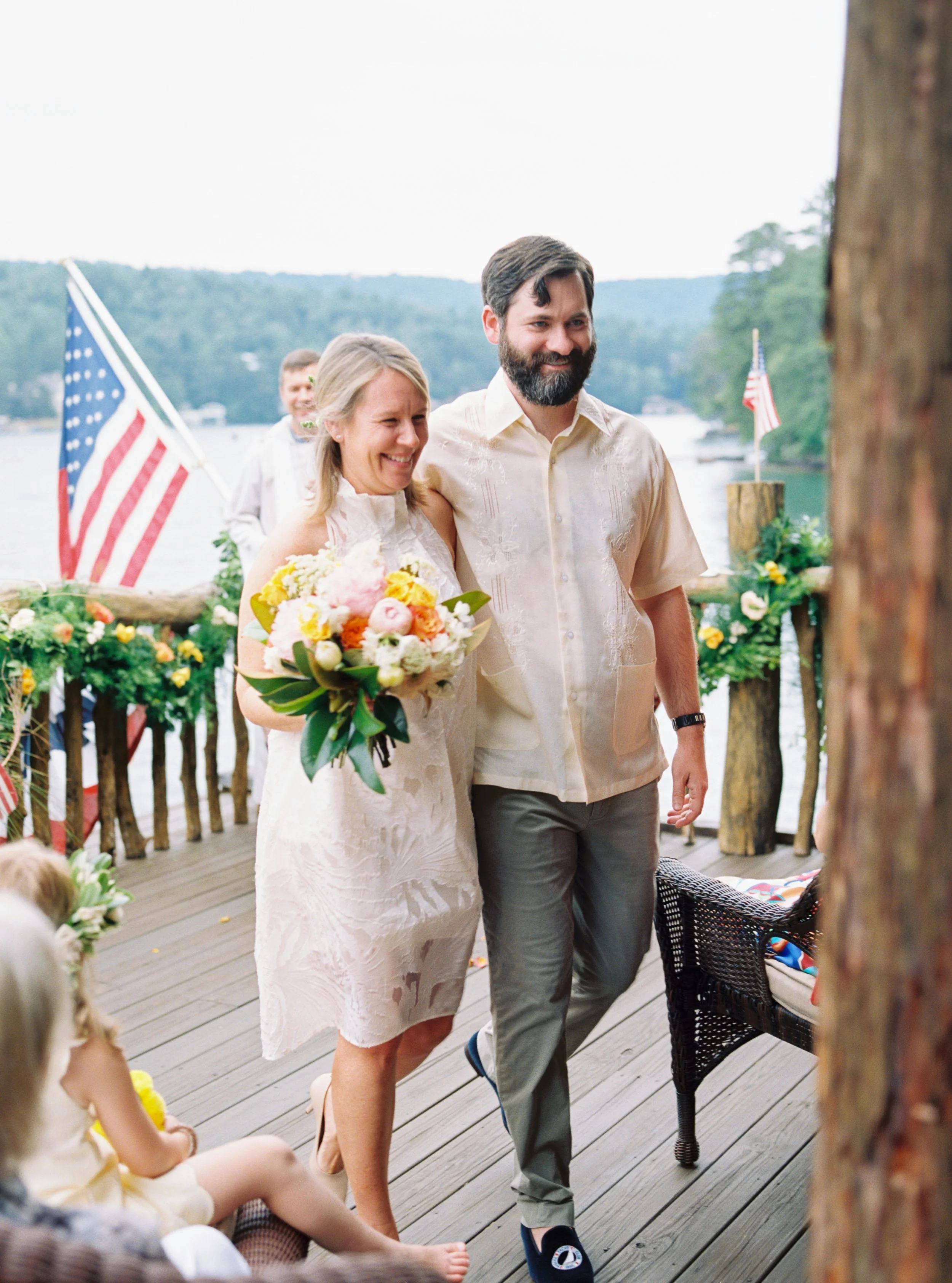 Bride and groom posing together with their dog on a wooden deck decorated with an American flag