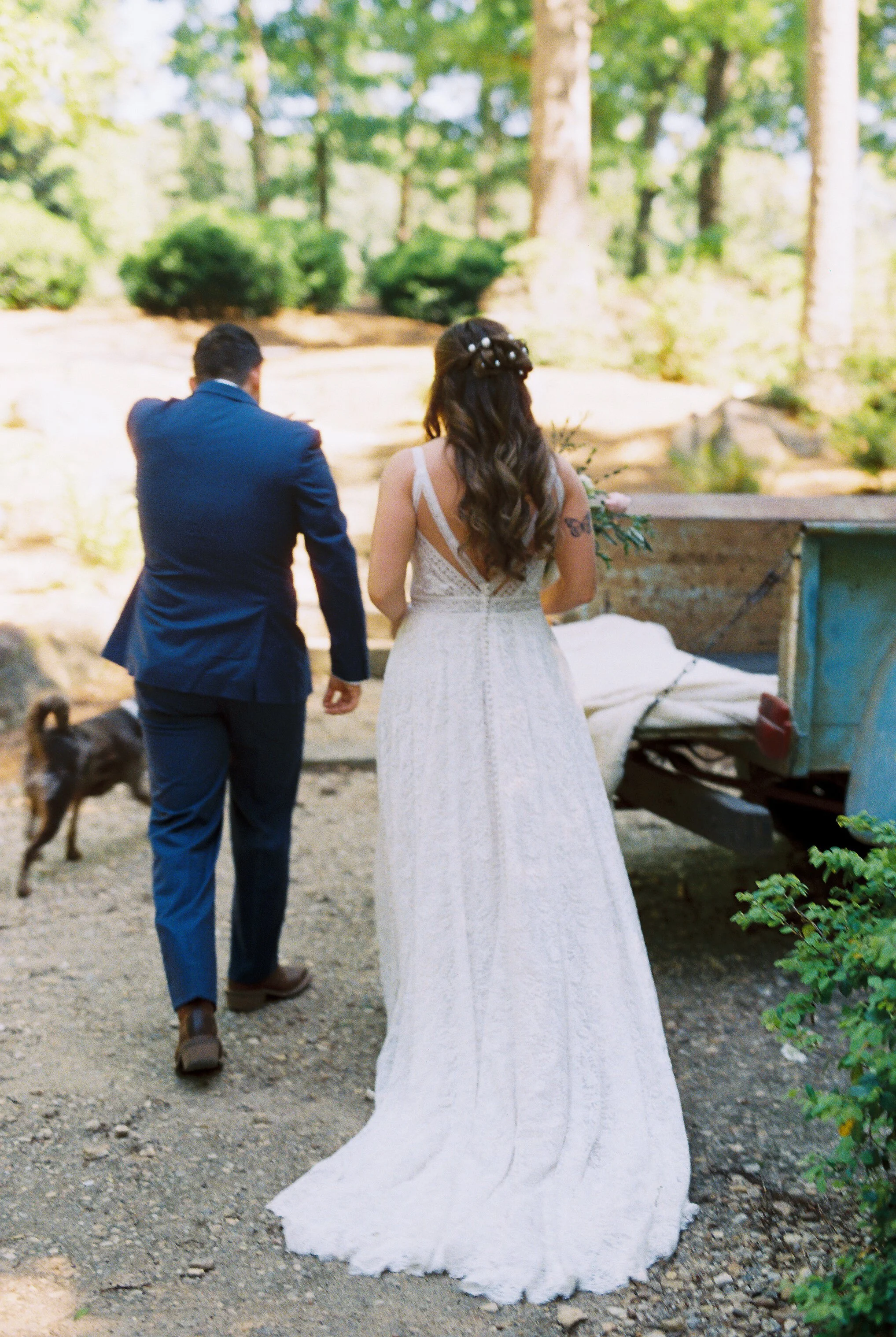 Bride and groom walking hand in hand down a wooded path after the ceremony, with Dakota the dog following behind