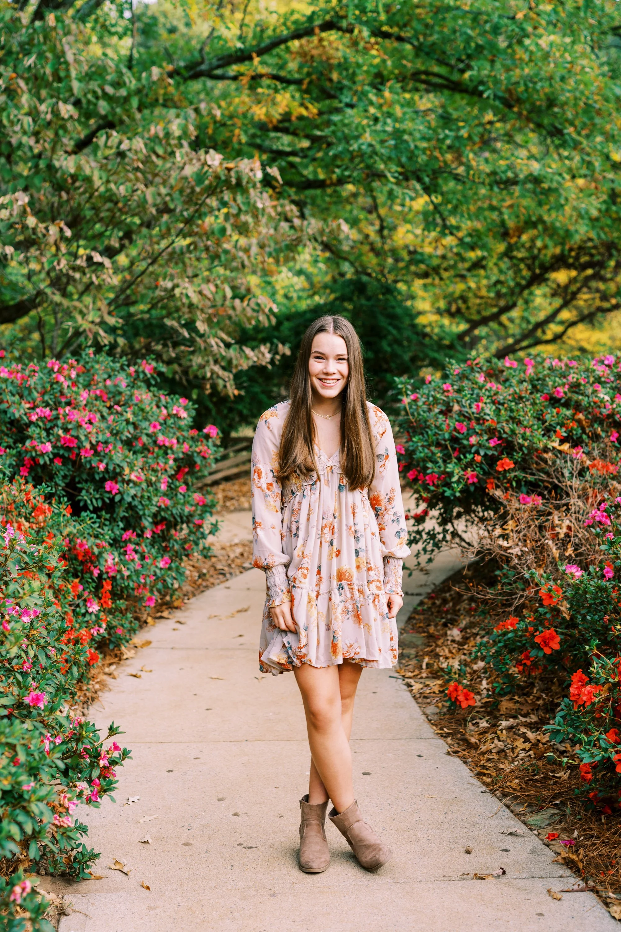 Full-length senior portrait of Hannah standing on a garden path lined with flowers in a floral dress at Kennesaw Mountain Battlefield Park in Kennesaw, Georgia