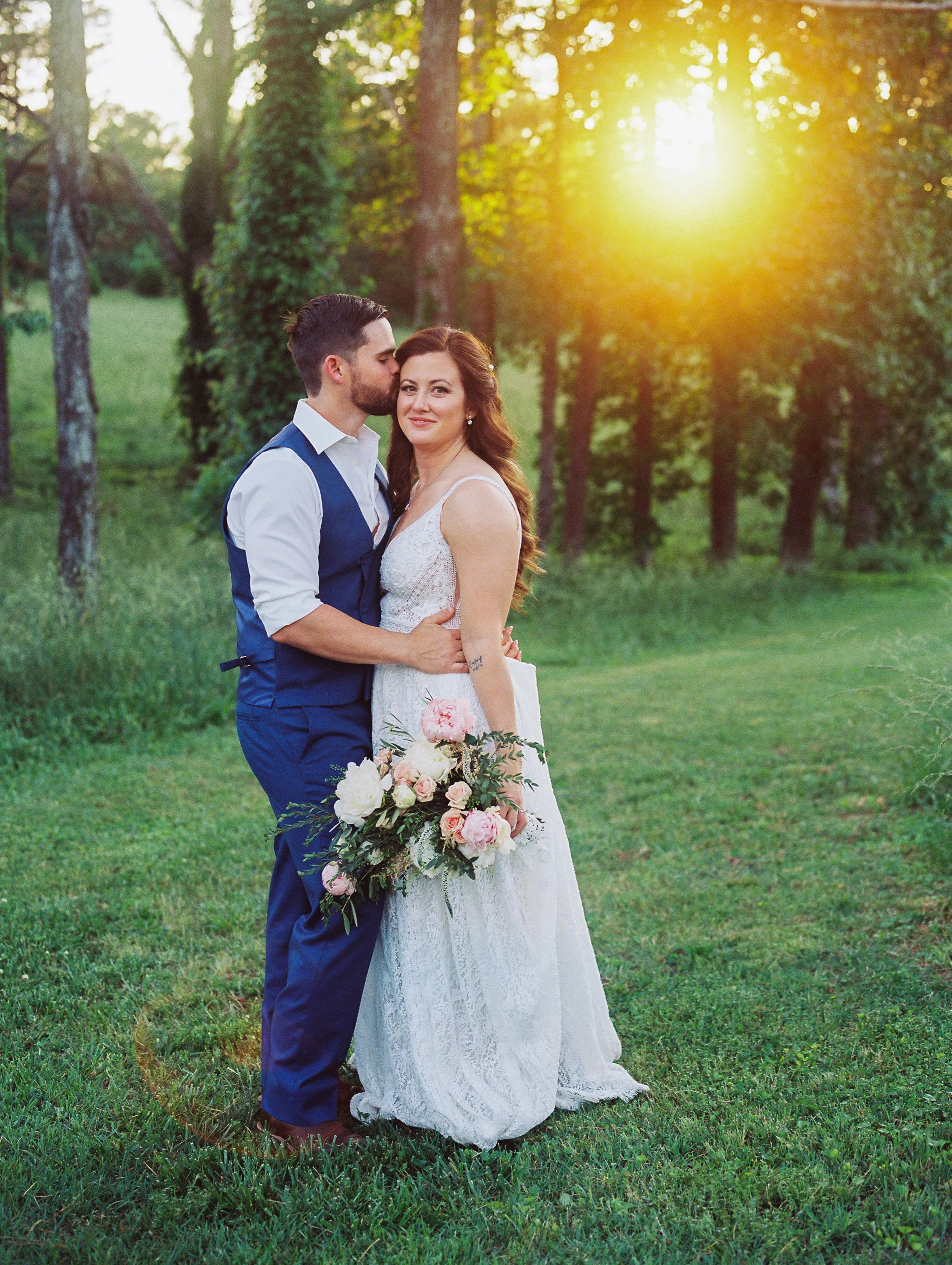 Bride and groom standing together in a sunlit field at golden hour, bride holding her bouquet