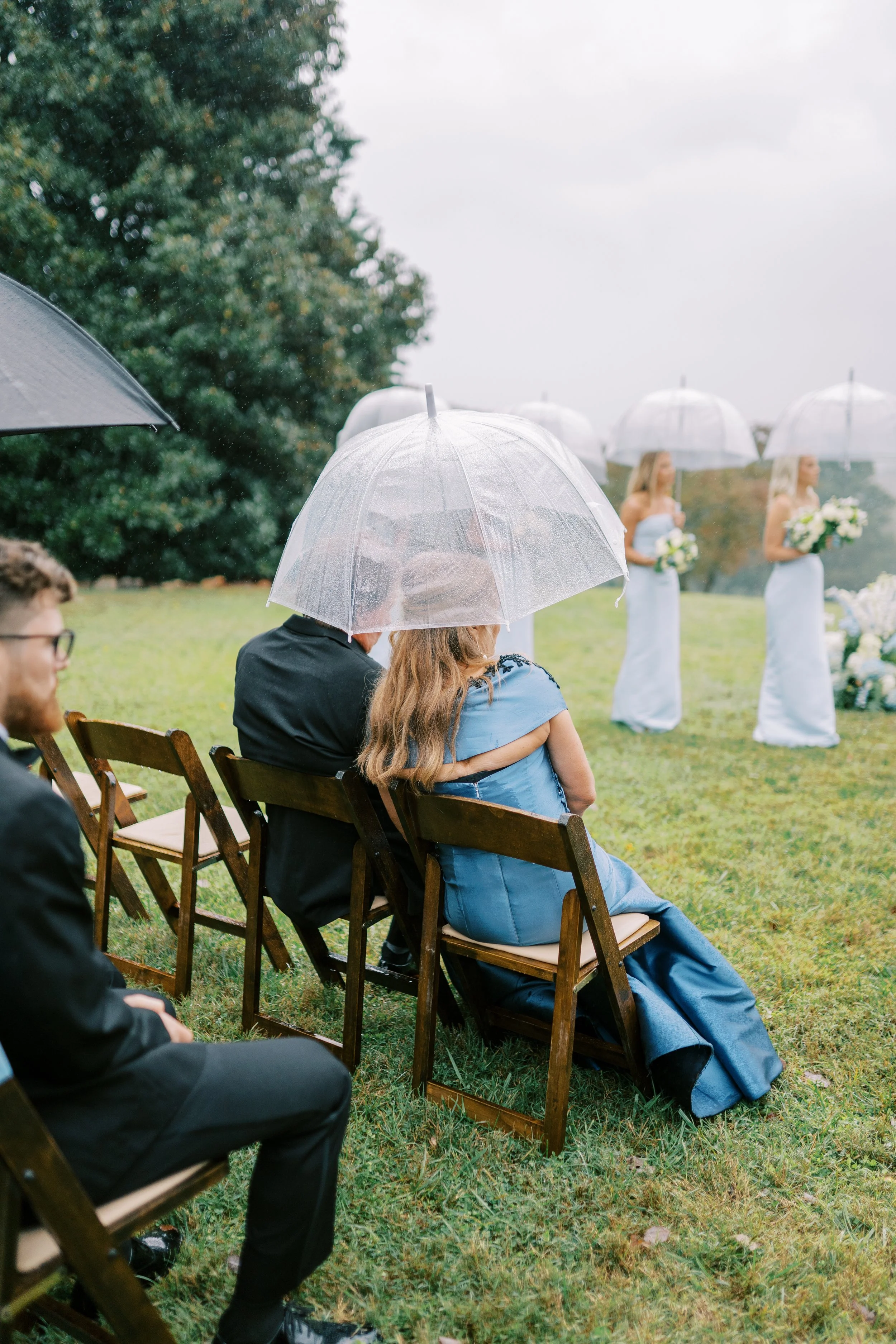 Bride's parents seated at the ceremony holding an umbrella