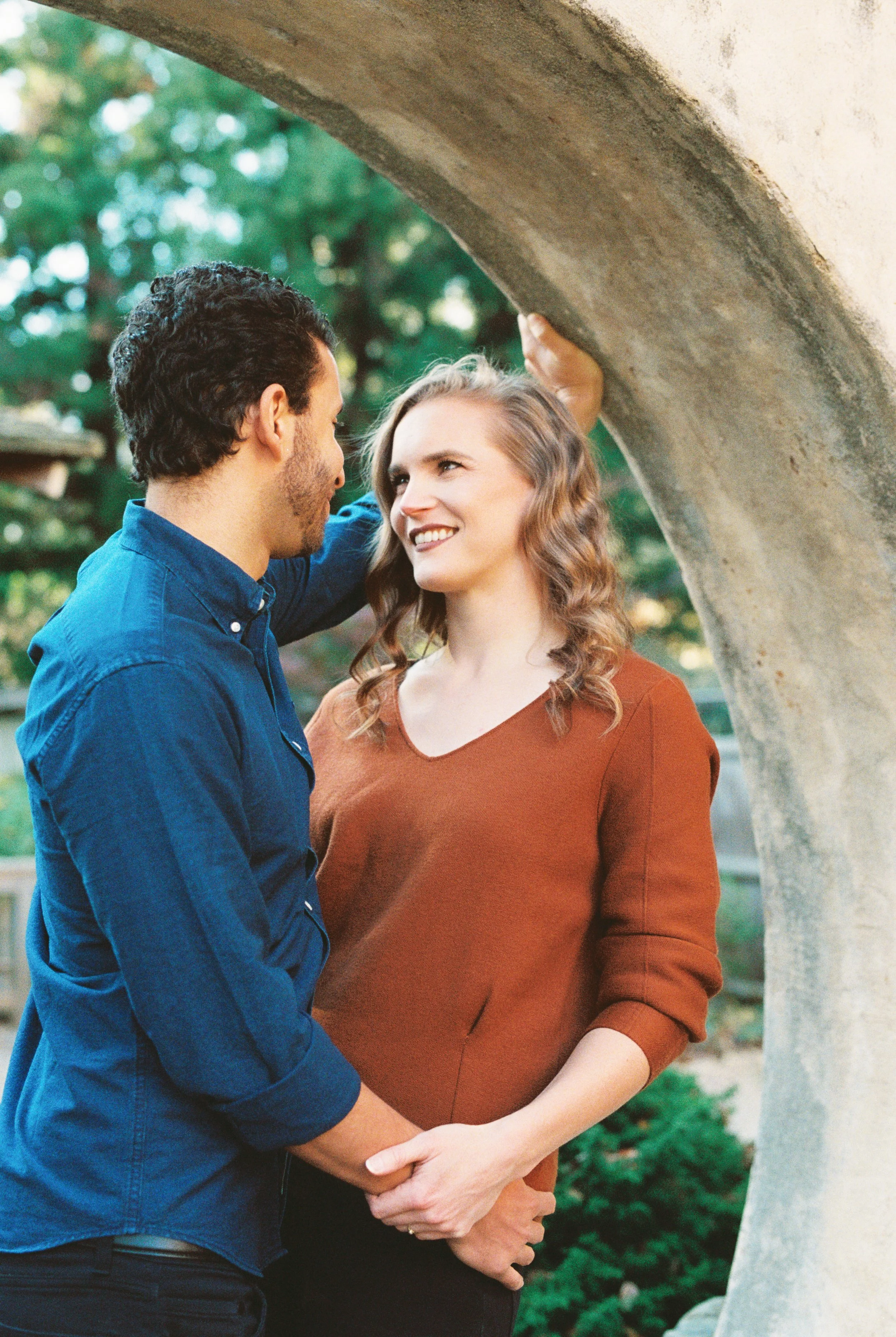 Couple sharing a tender moment beneath a stone archway, he touches her hair