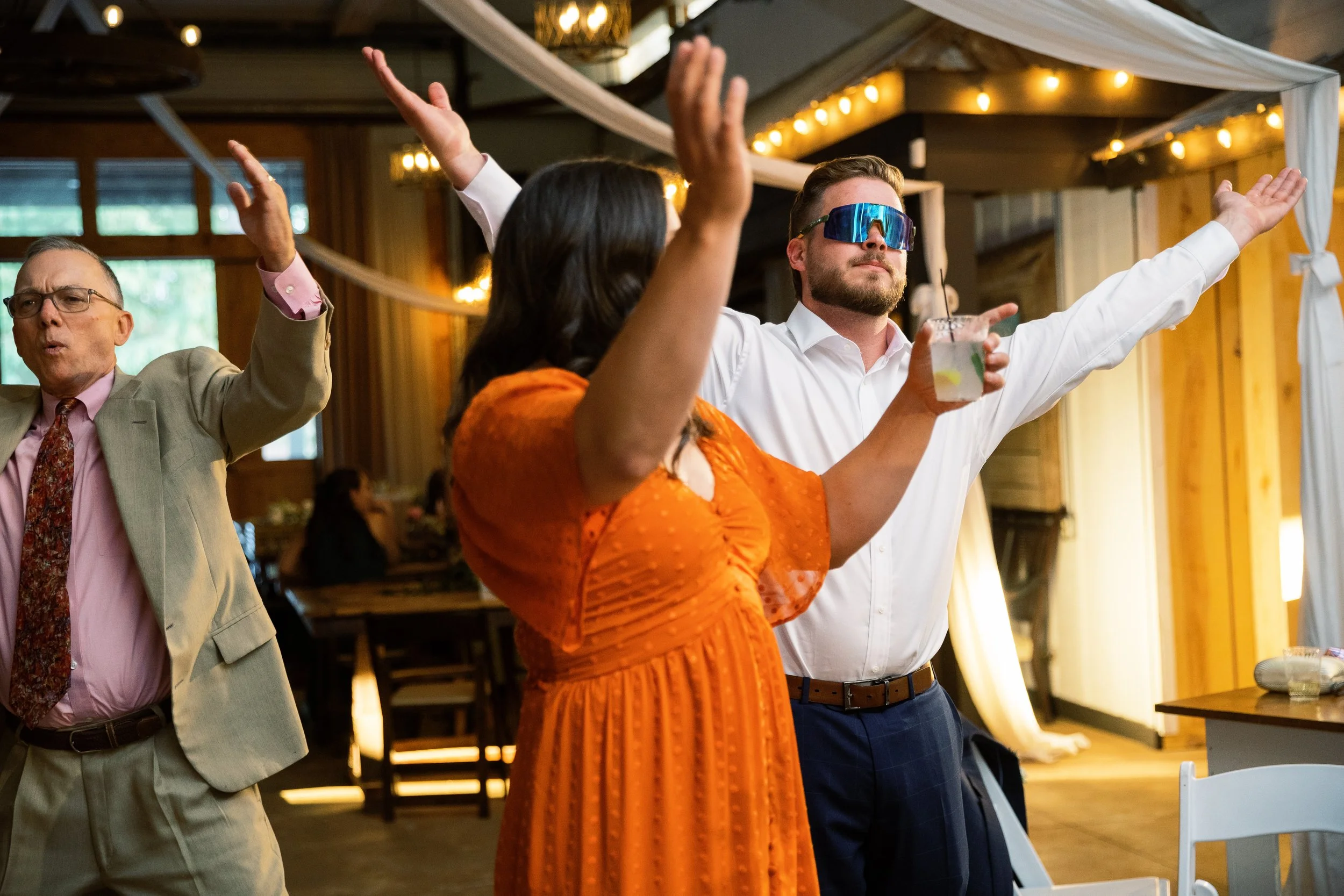 Guests dancing with hands raised under string lights during the reception