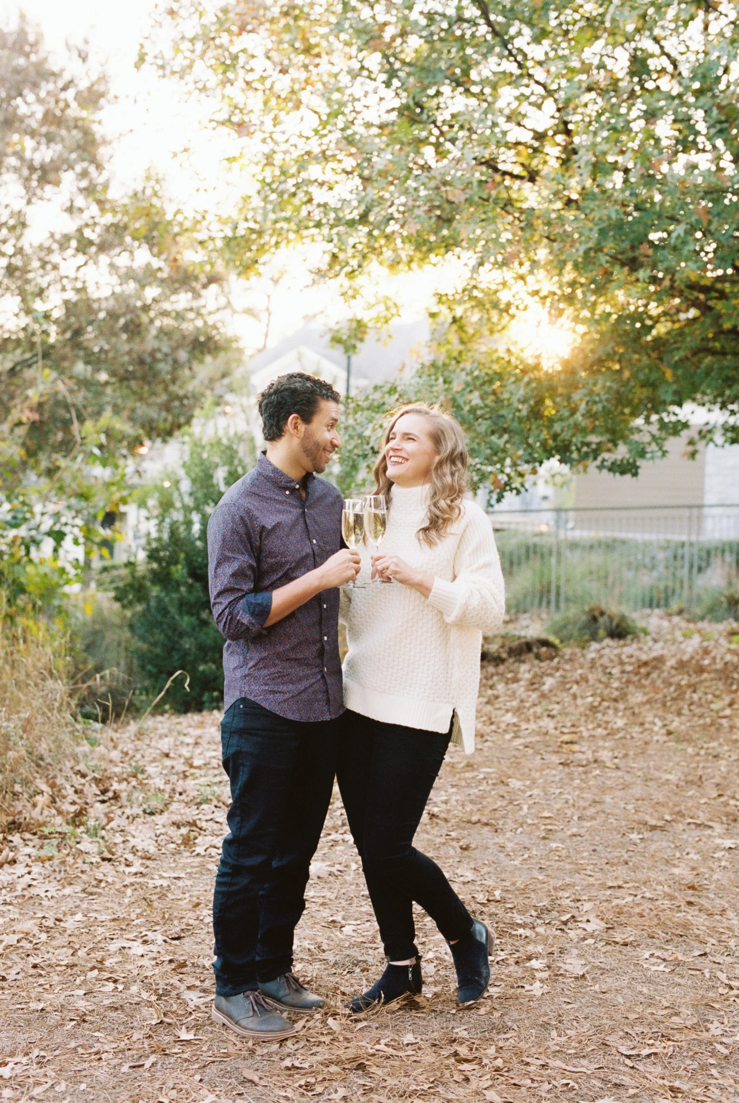Engaged couple toasting champagne glasses together on a sunlit garden path at Atlanta Botanical Garden