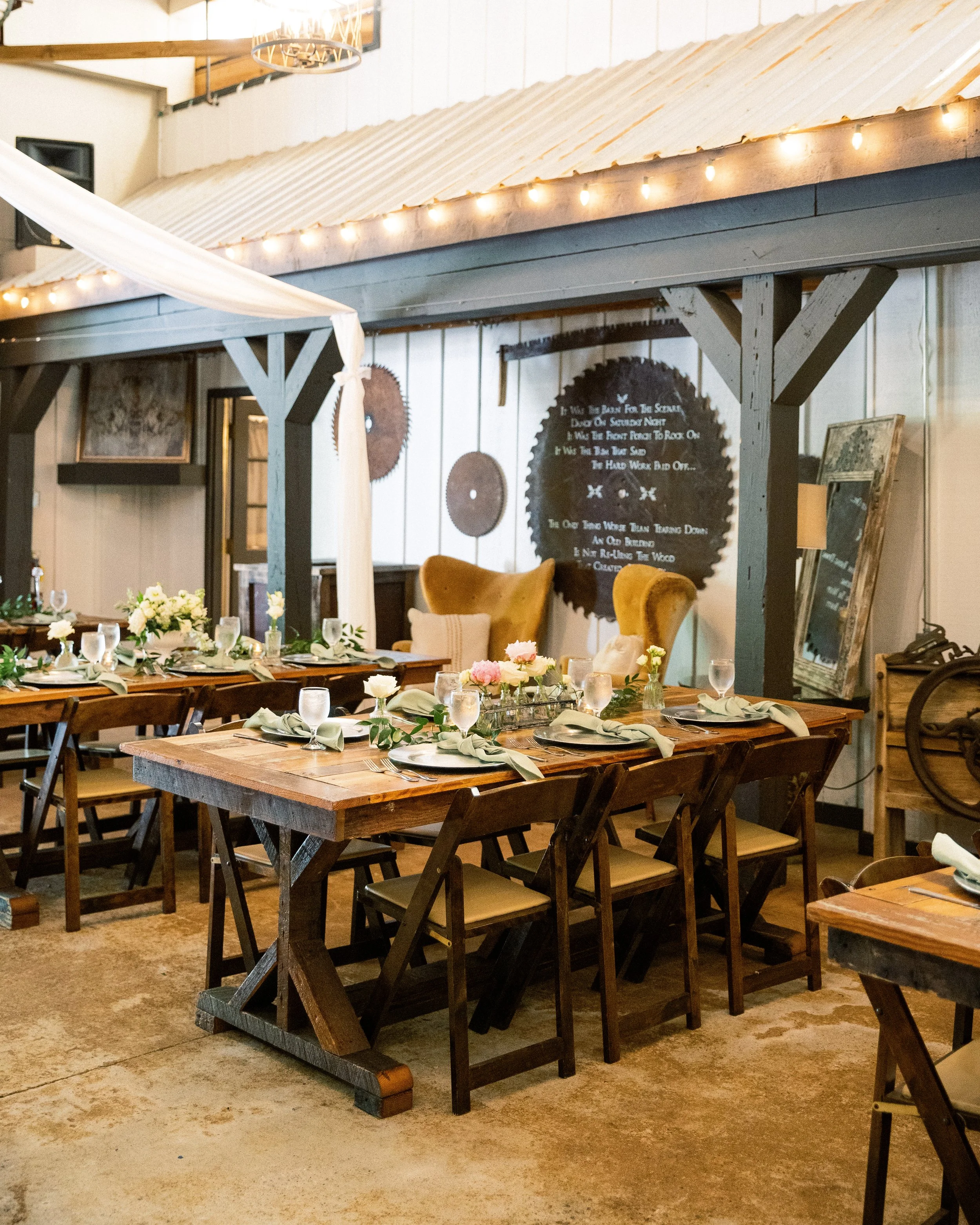 Reception dining tables set with string lights overhead in the barn-style venue