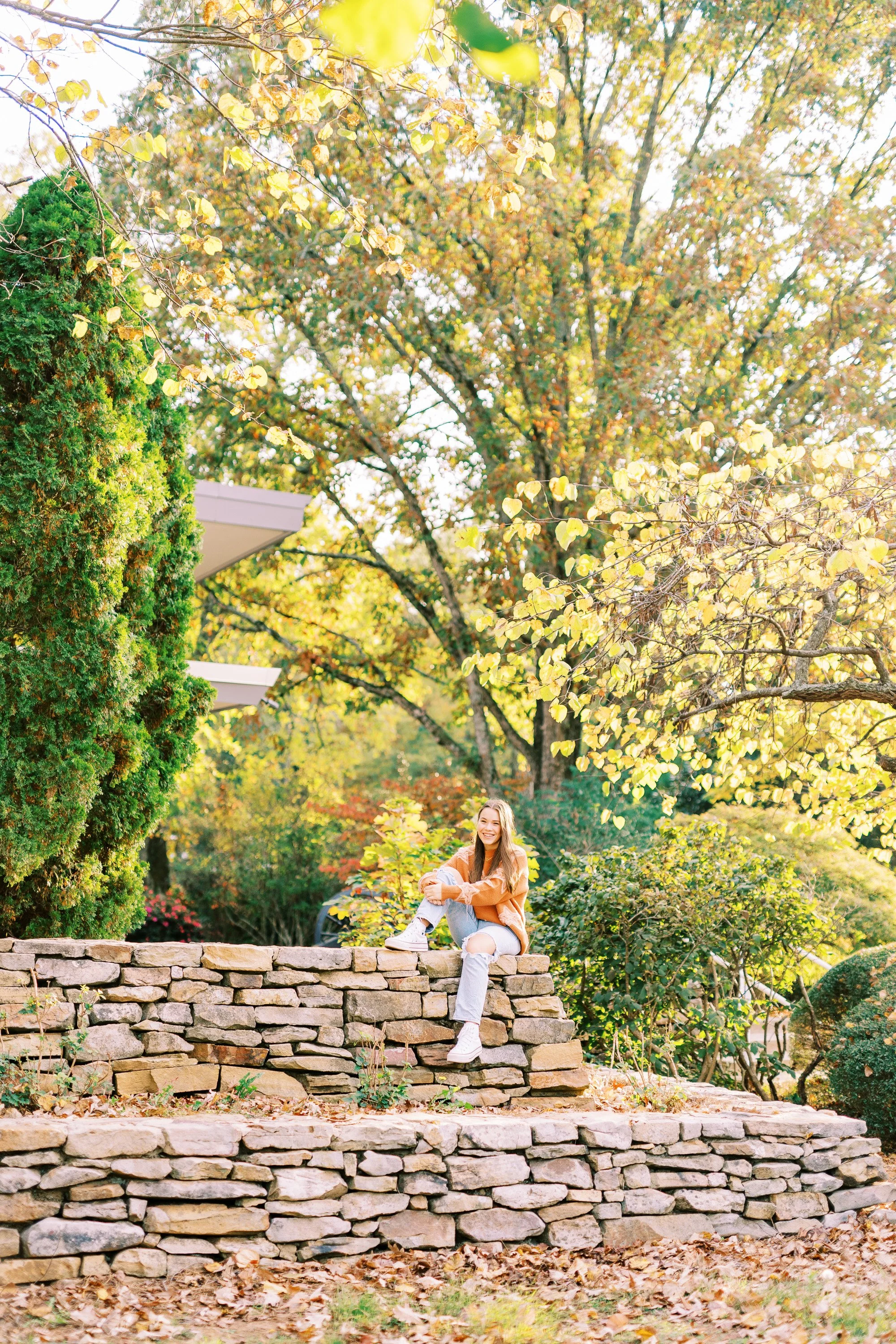 Senior portrait of Hannah sitting on a stone wall in an orange sweater at Kennesaw Mountain Battlefield Park in Kennesaw, Georgia