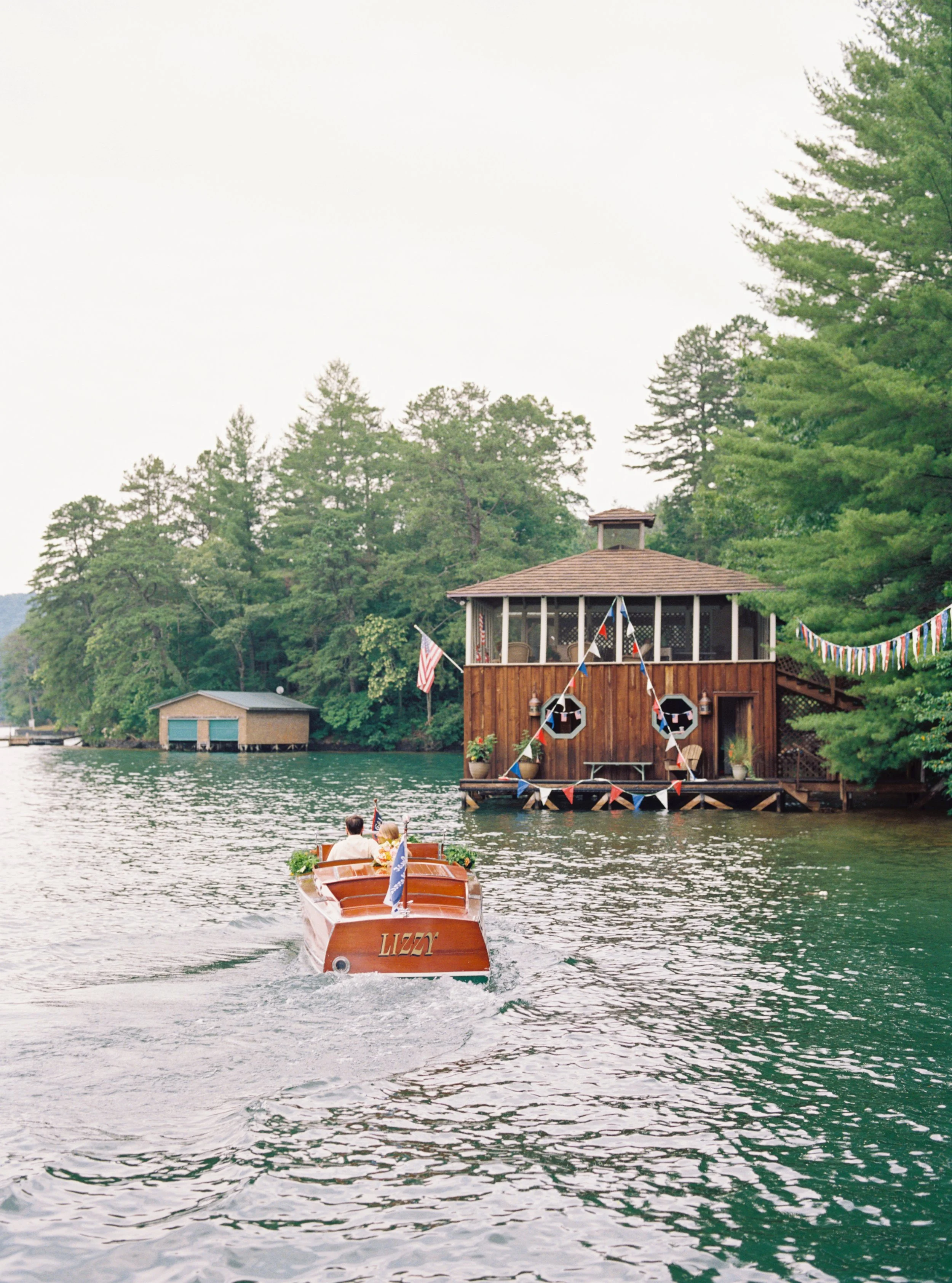 Small wooden boat approaching a lakeside boathouse framed by trees at Lake Rabun
