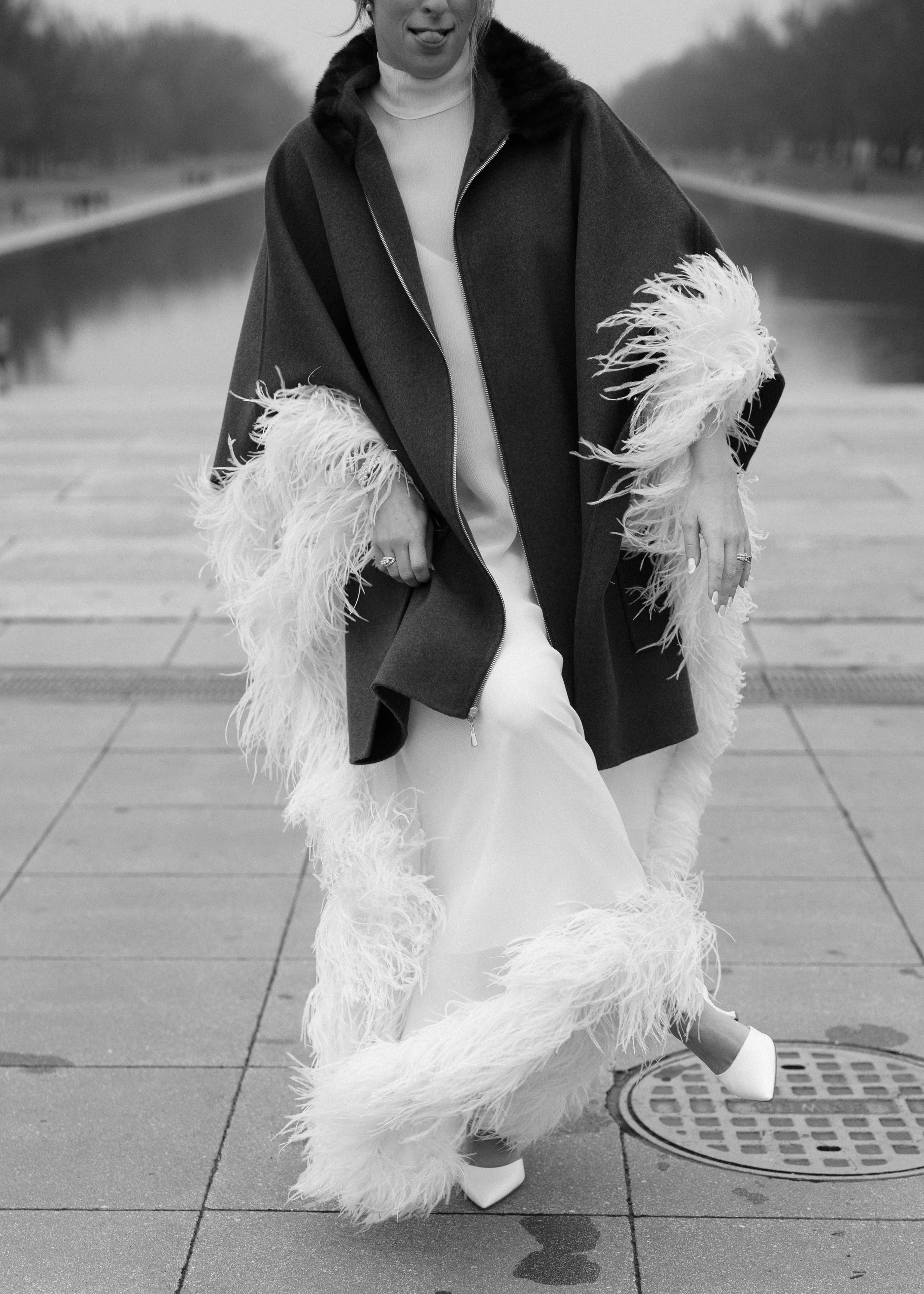 Black and white photo of the bride's feathered dress and cape from behind