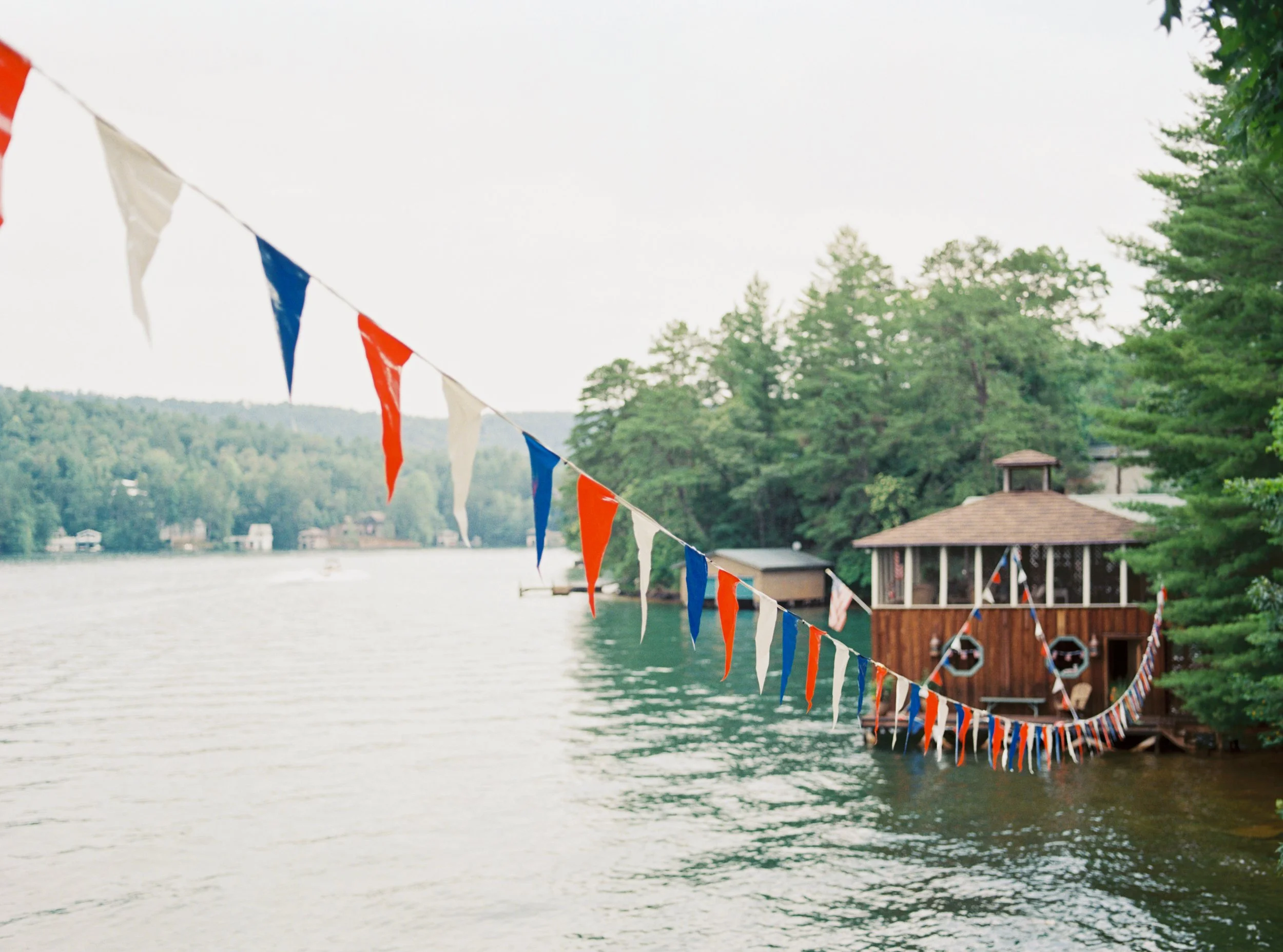 Colorful bunting flags strung across the water in front of a lakeside boathouse