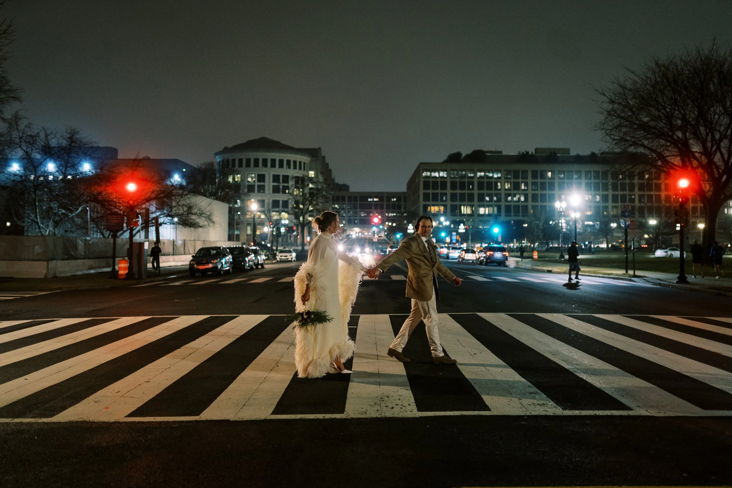 Bride and groom crossing a crosswalk at night with the illuminated Washington DC skyline behind them