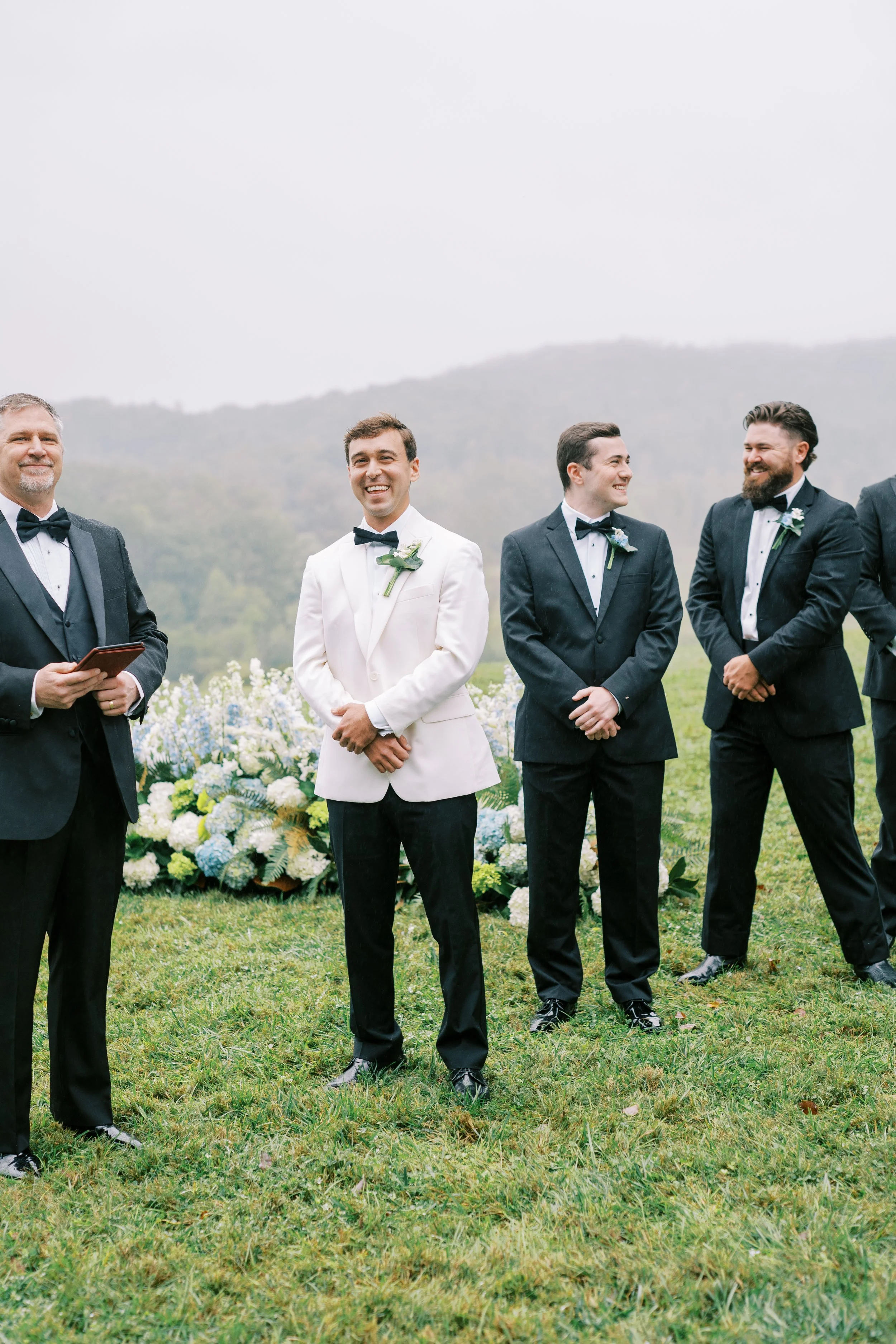 Groom and groomsmen standing at the ceremony floral arch
