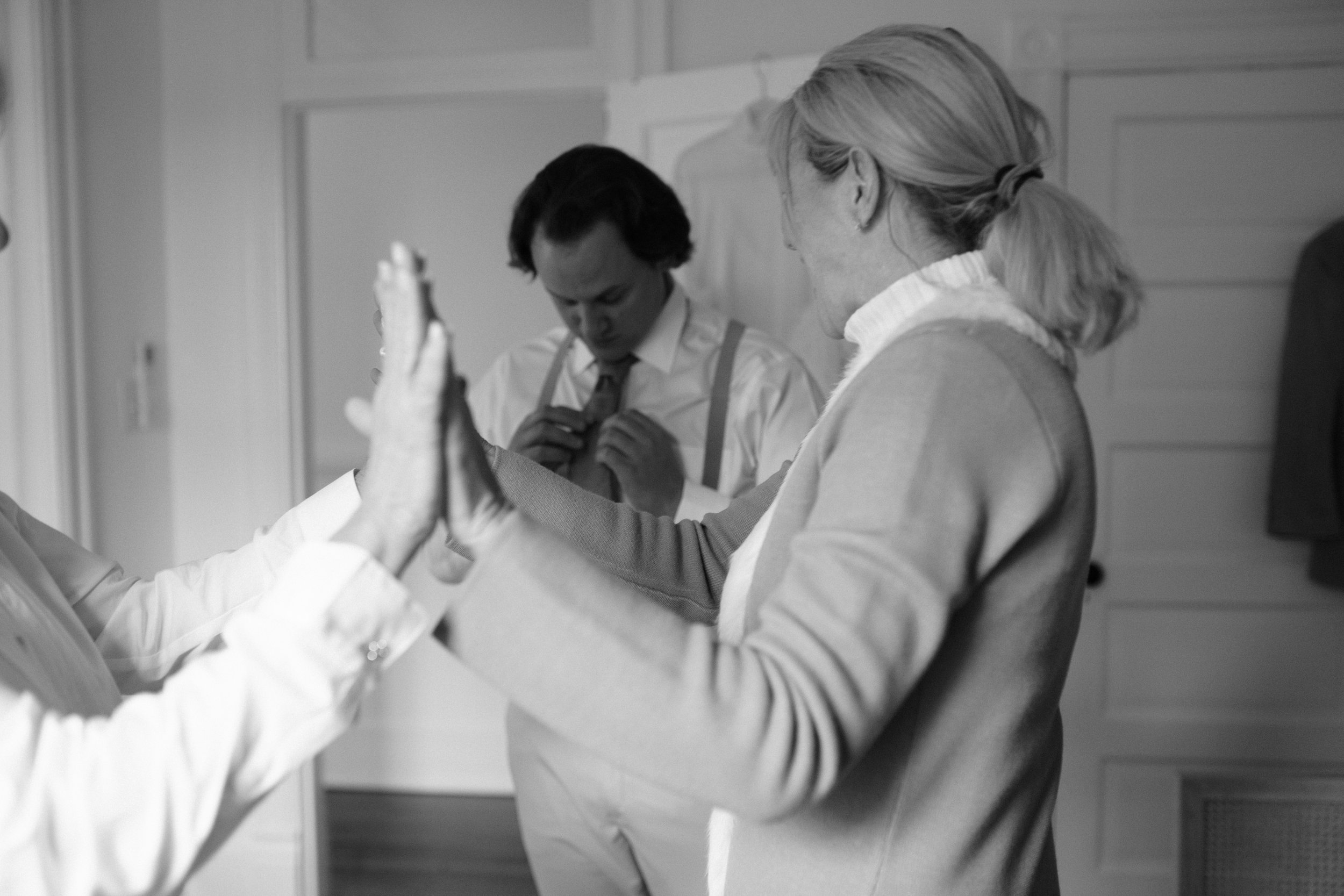 Black and white photo of the groom having his tie adjusted while getting ready