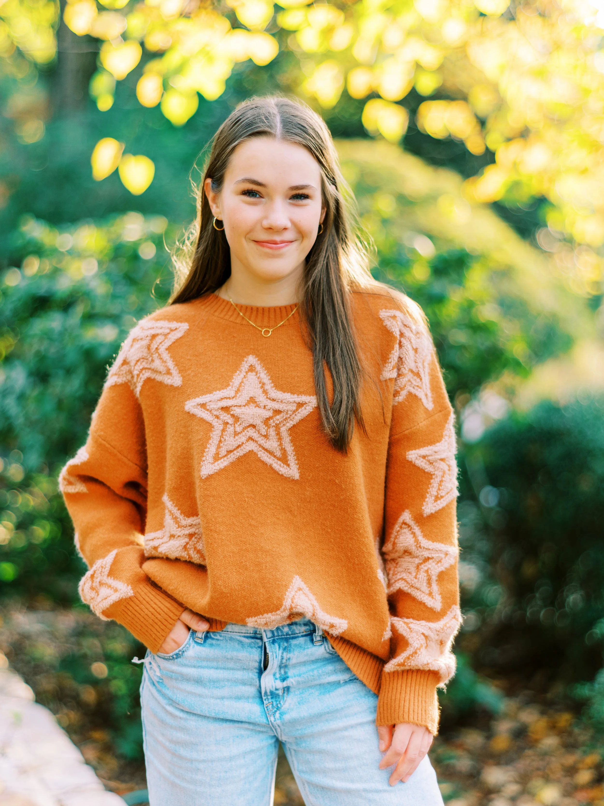 Senior portrait of Hannah standing with hands in her pockets wearing an orange star-patterned sweater at Kennesaw Mountain Battlefield Park in Kennesaw, Georgia