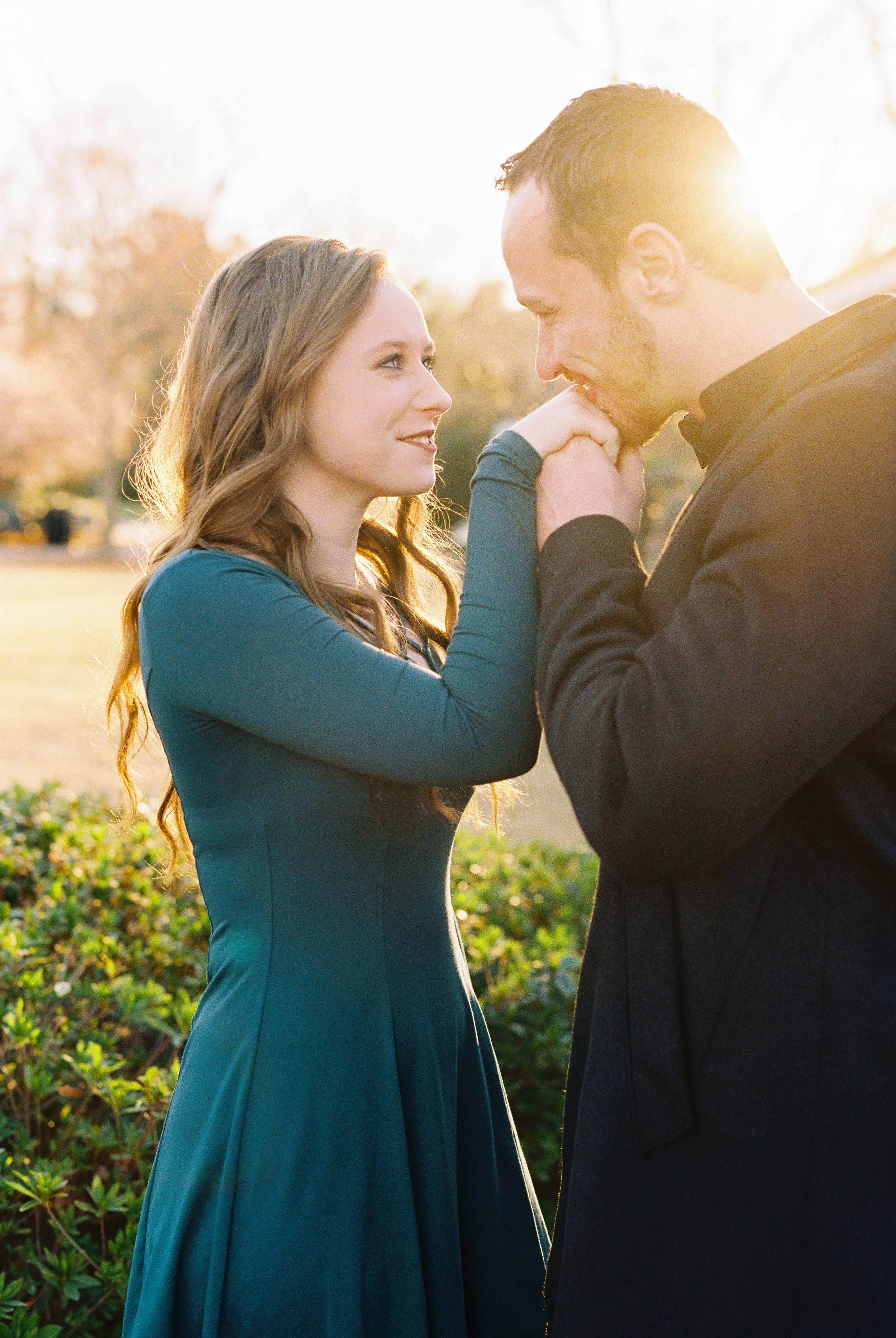 Conner and Maddie share a close embrace as he kisses her hand in golden hour light during their engagement session in Dallas, Georgia.