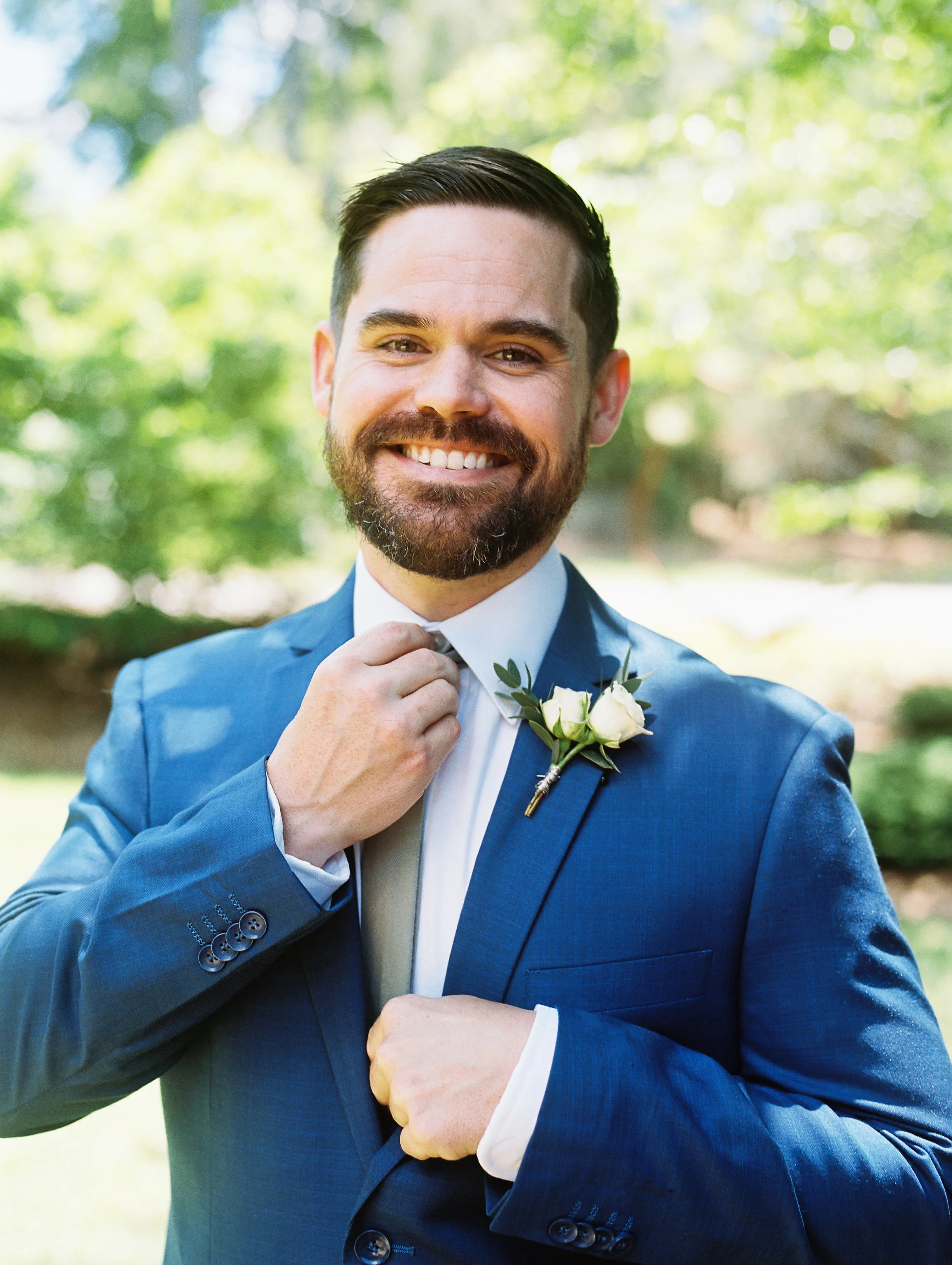 Groom smiling and adjusting his boutonniere while getting ready