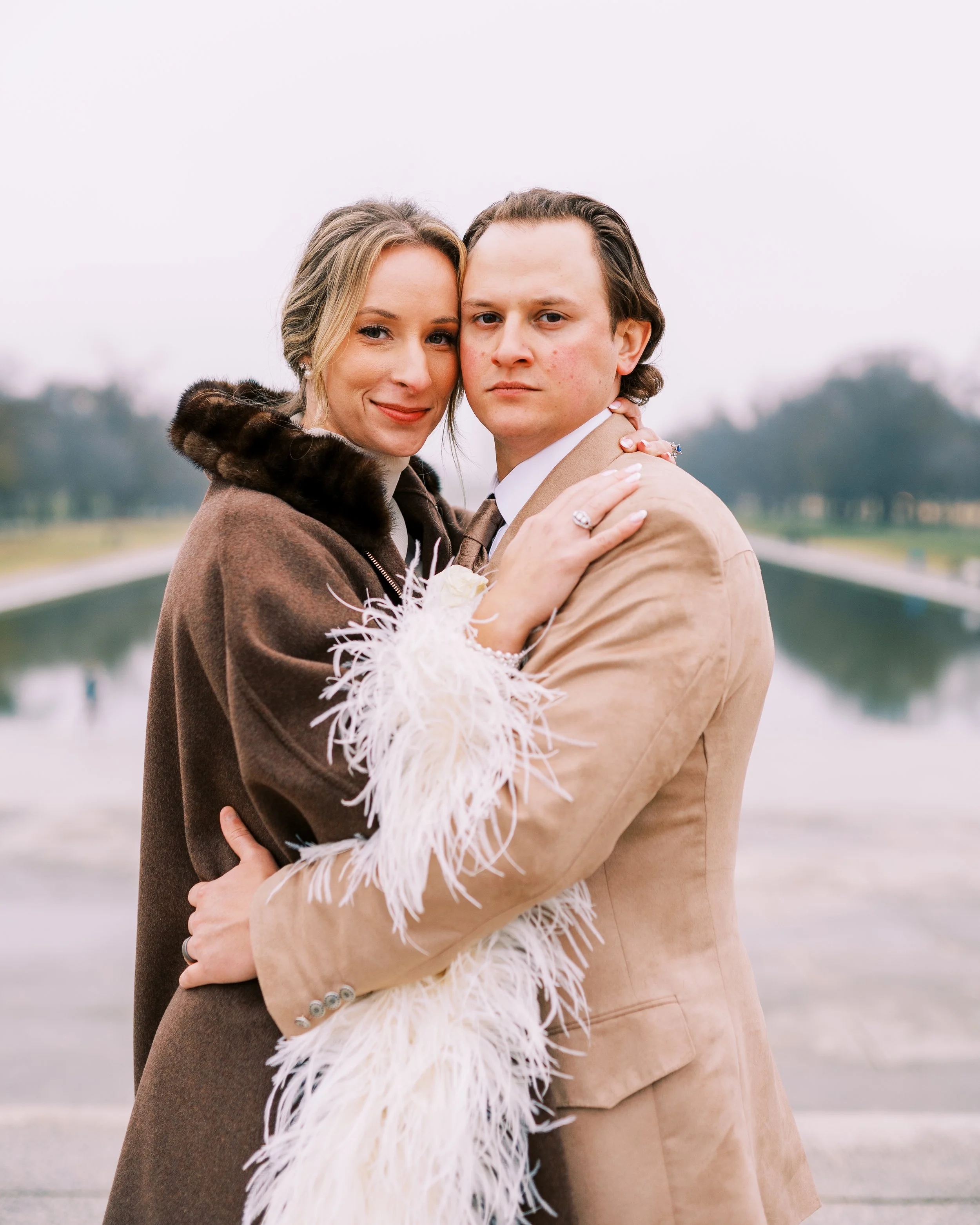 Bride and groom embracing closely with the reflecting pool and monument in the background