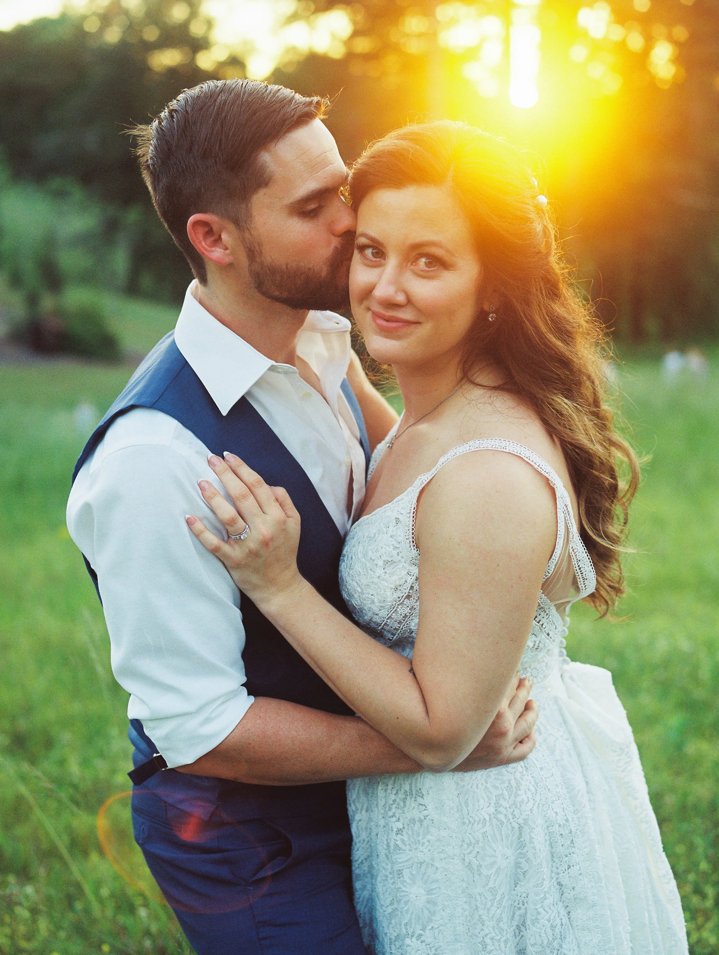 Groom kissing the bride's cheek as she smiles, golden sunset light behind them