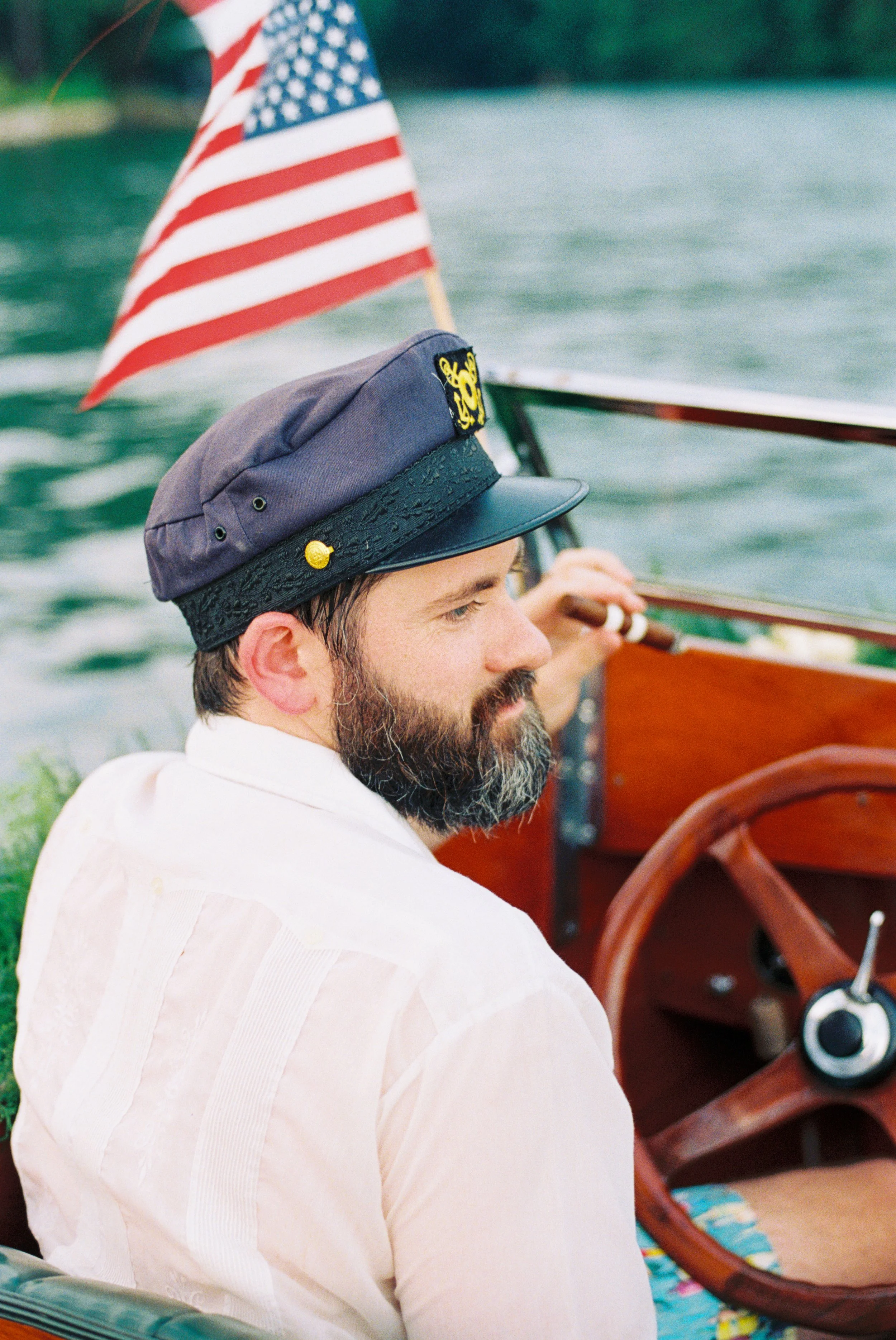 Boat captain in a nautical hat steering the wooden boat with an American flag mounted on the bow