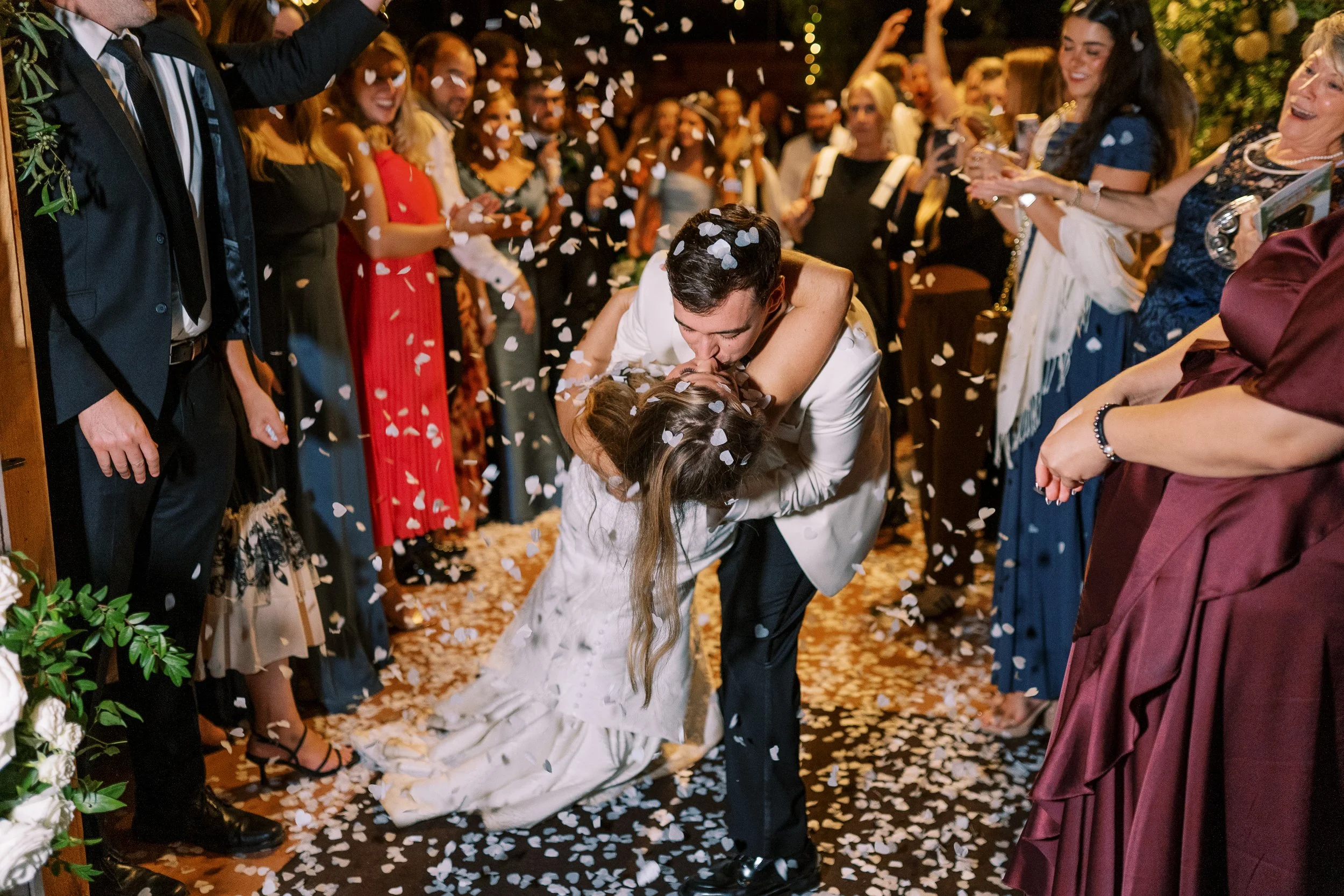 Groom dipping bride during confetti sendoff at night