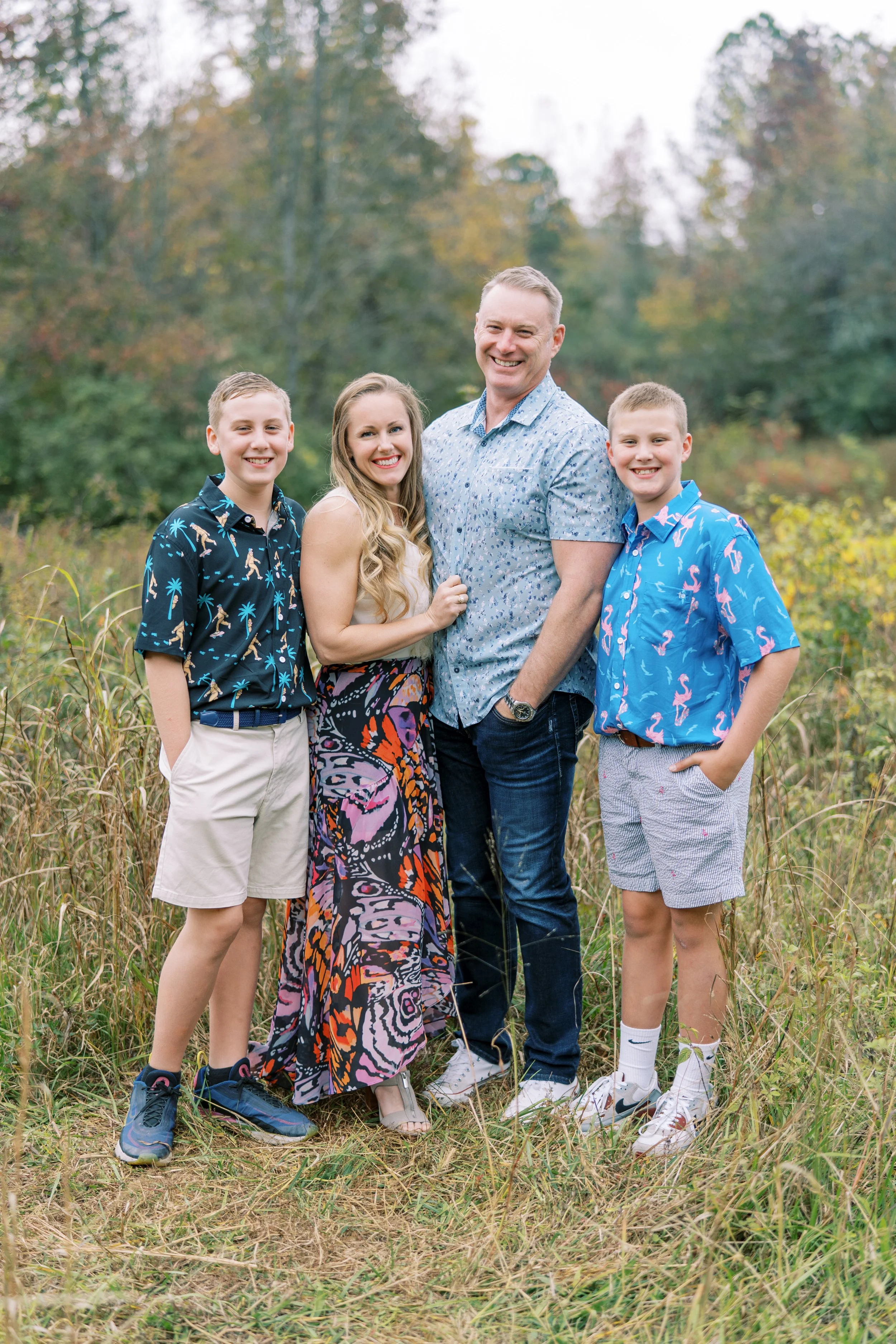 Family portrait outdoors with three children and two adults, walking in a grassy field with trees in the background.