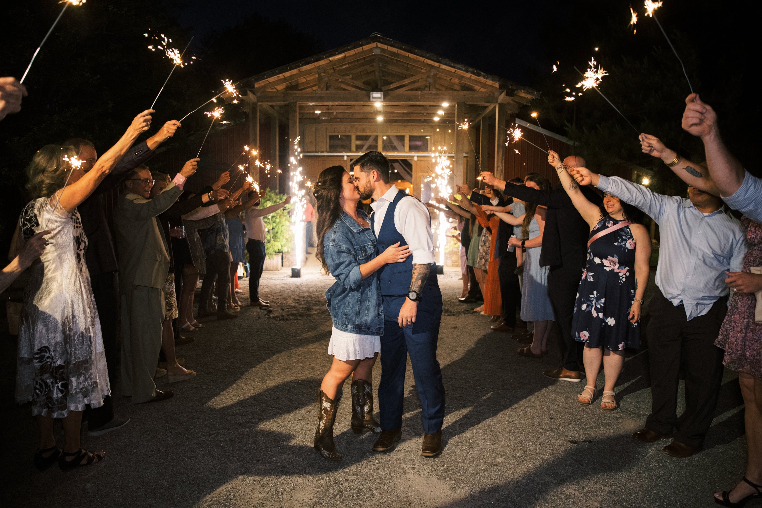 Bride and groom running through a sparkler send-off tunnel of cheering guests
