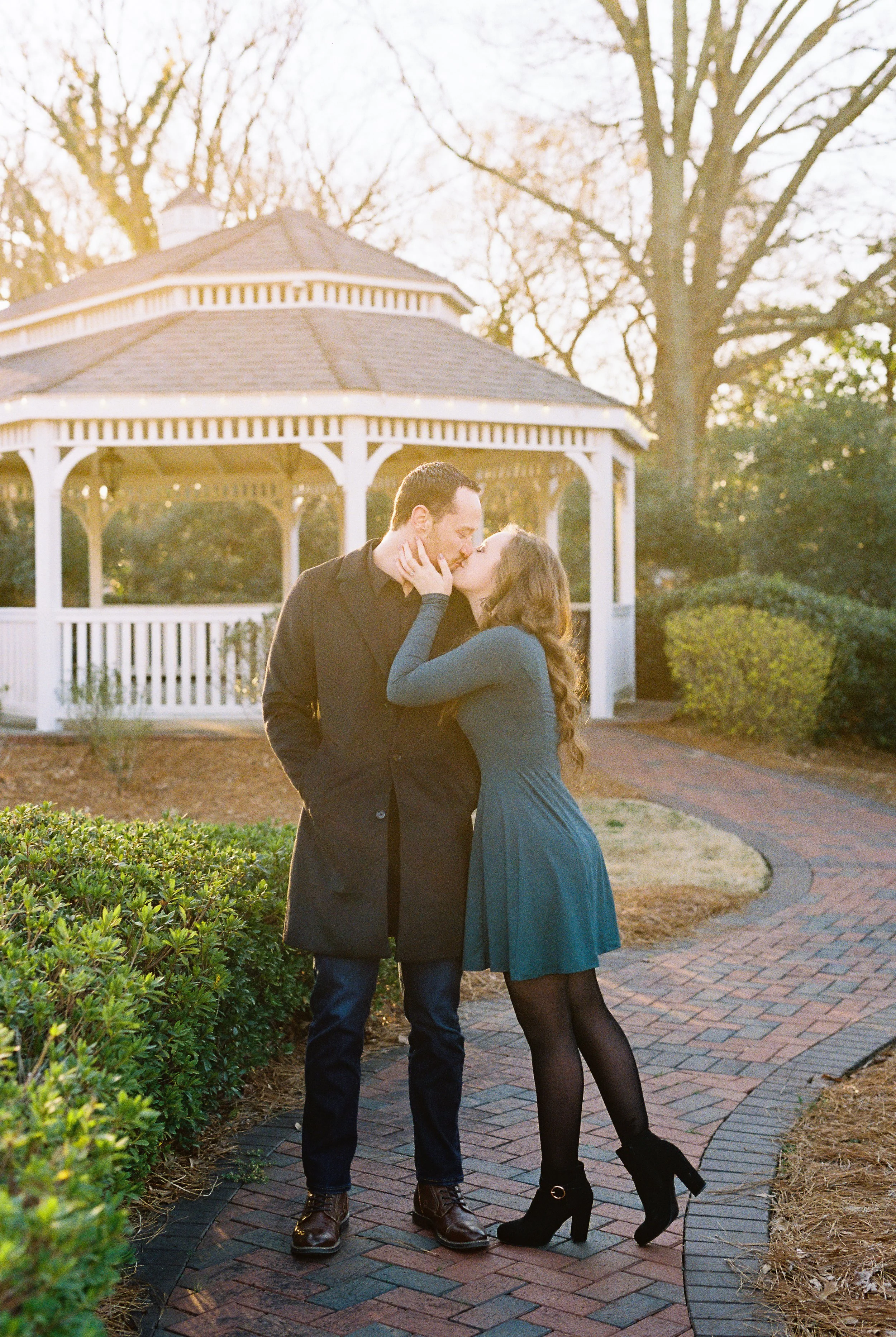 Conner and Maddie share a kiss in front of a white gazebo in a Dallas, Georgia park during their engagement session.