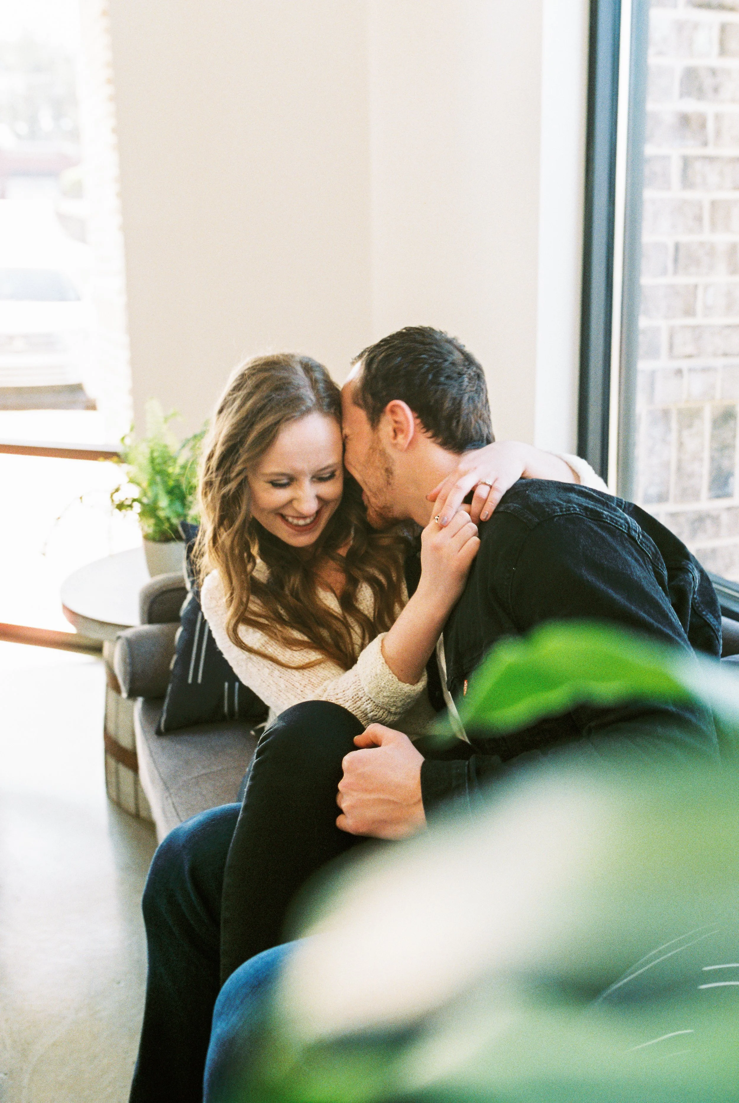 Maddie laughs brightly as Conner kisses her hair on a couch in a Dallas, Georgia coffee shop.