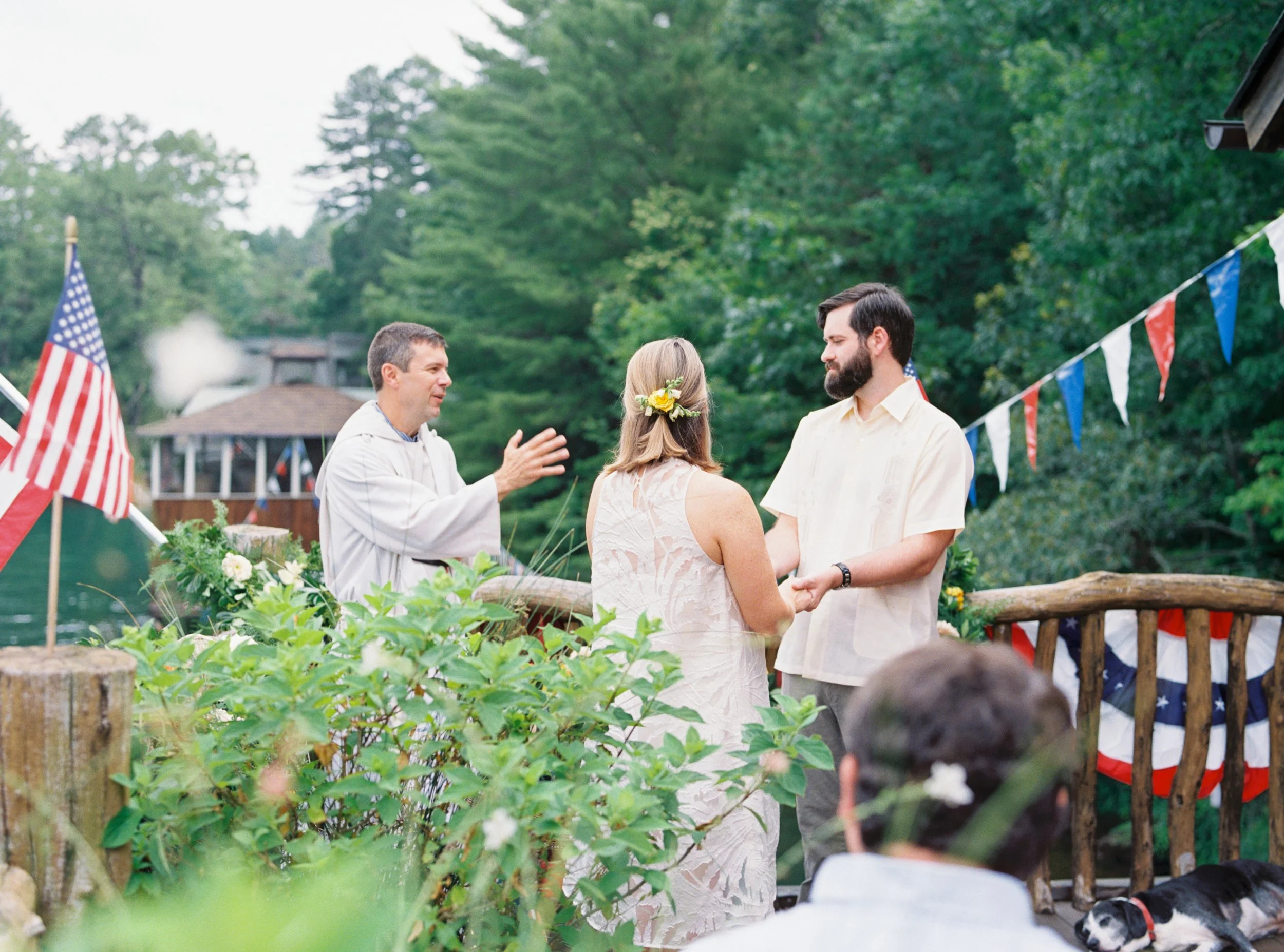 Officiant leading the couple through their vows at an outdoor lakeside ceremony decorated with American flags