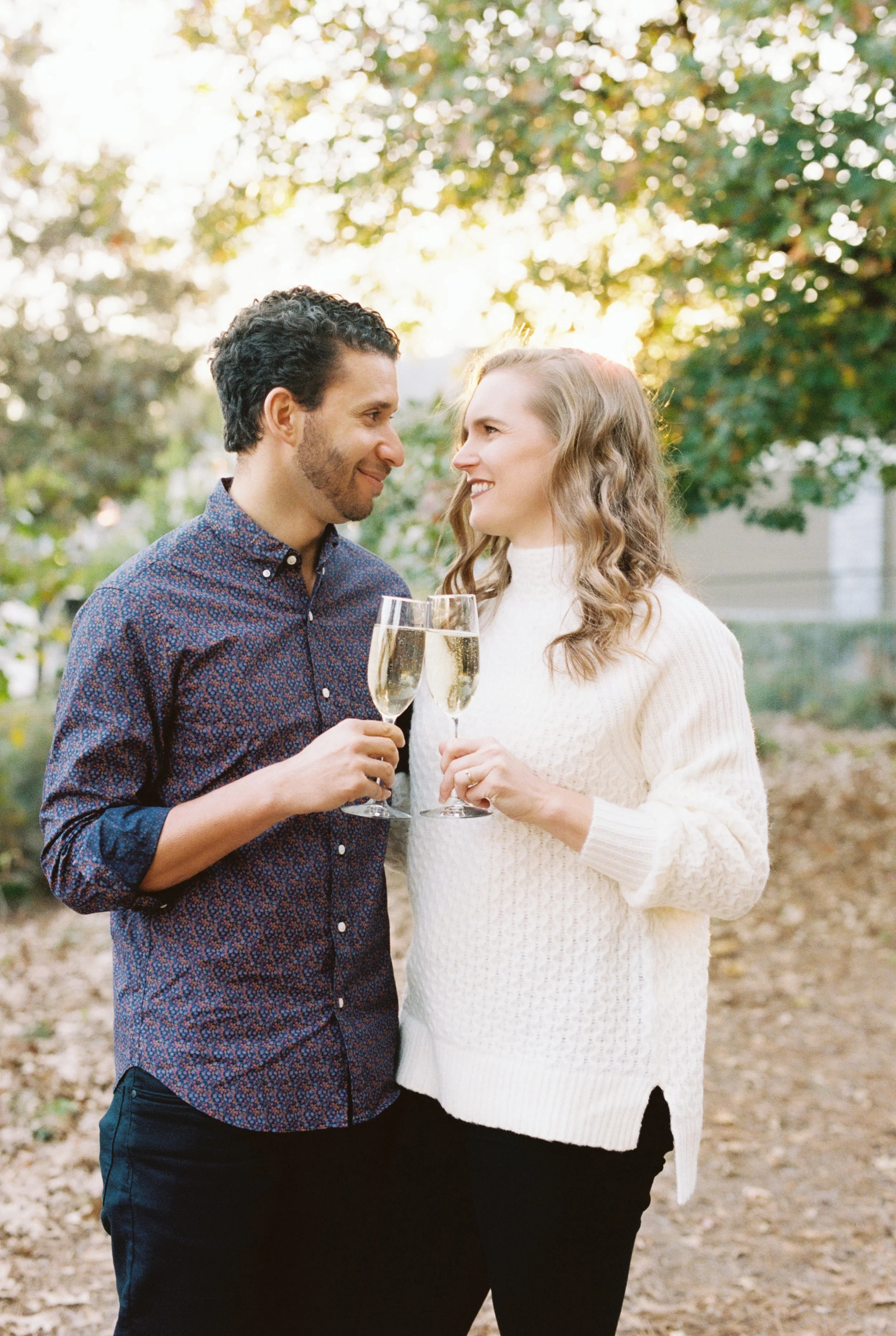 Engaged couple sharing a smile while holding champagne glasses in the garden