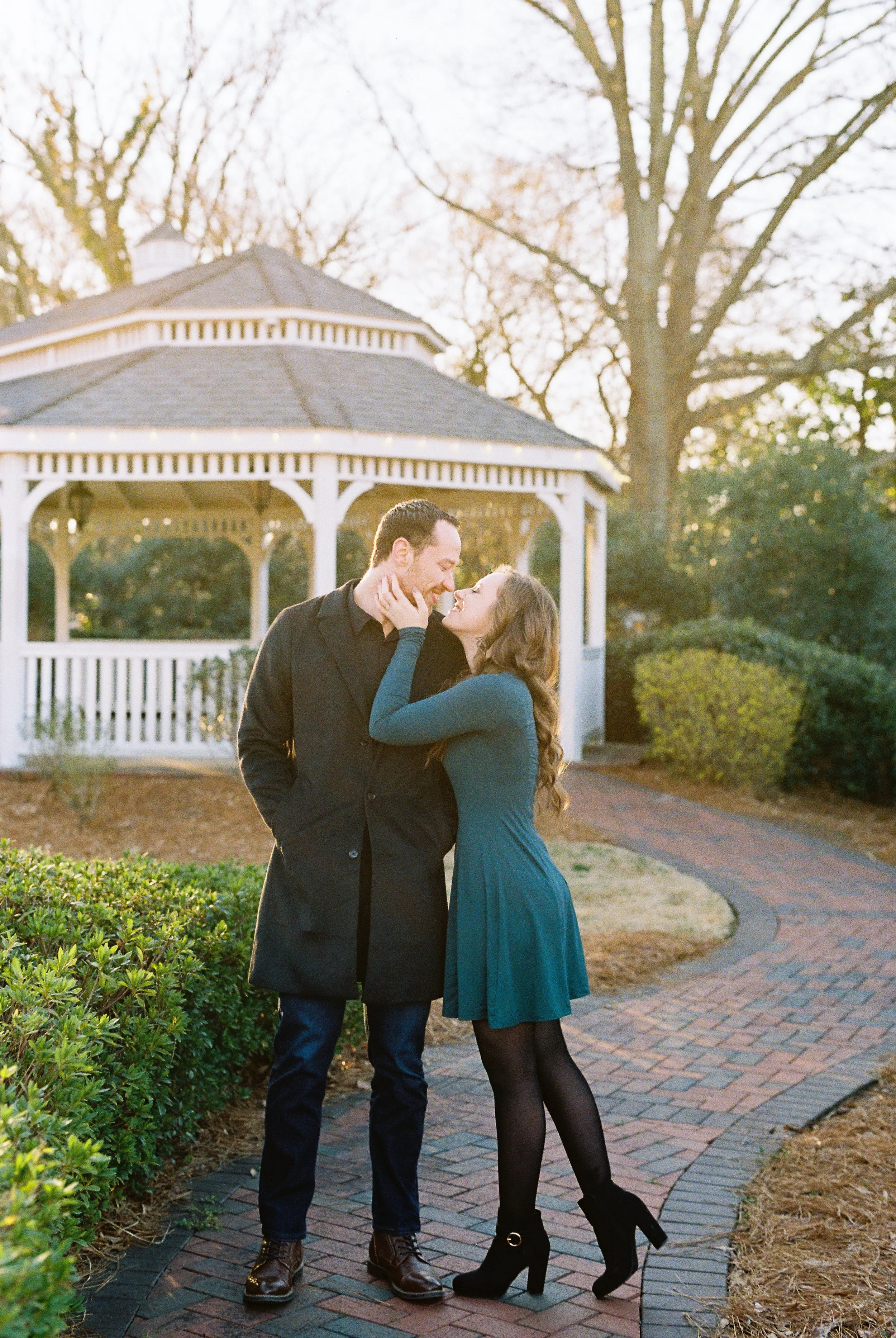 Conner and Maddie kiss on the brick path near a gazebo at golden hour in Dallas, Georgia.