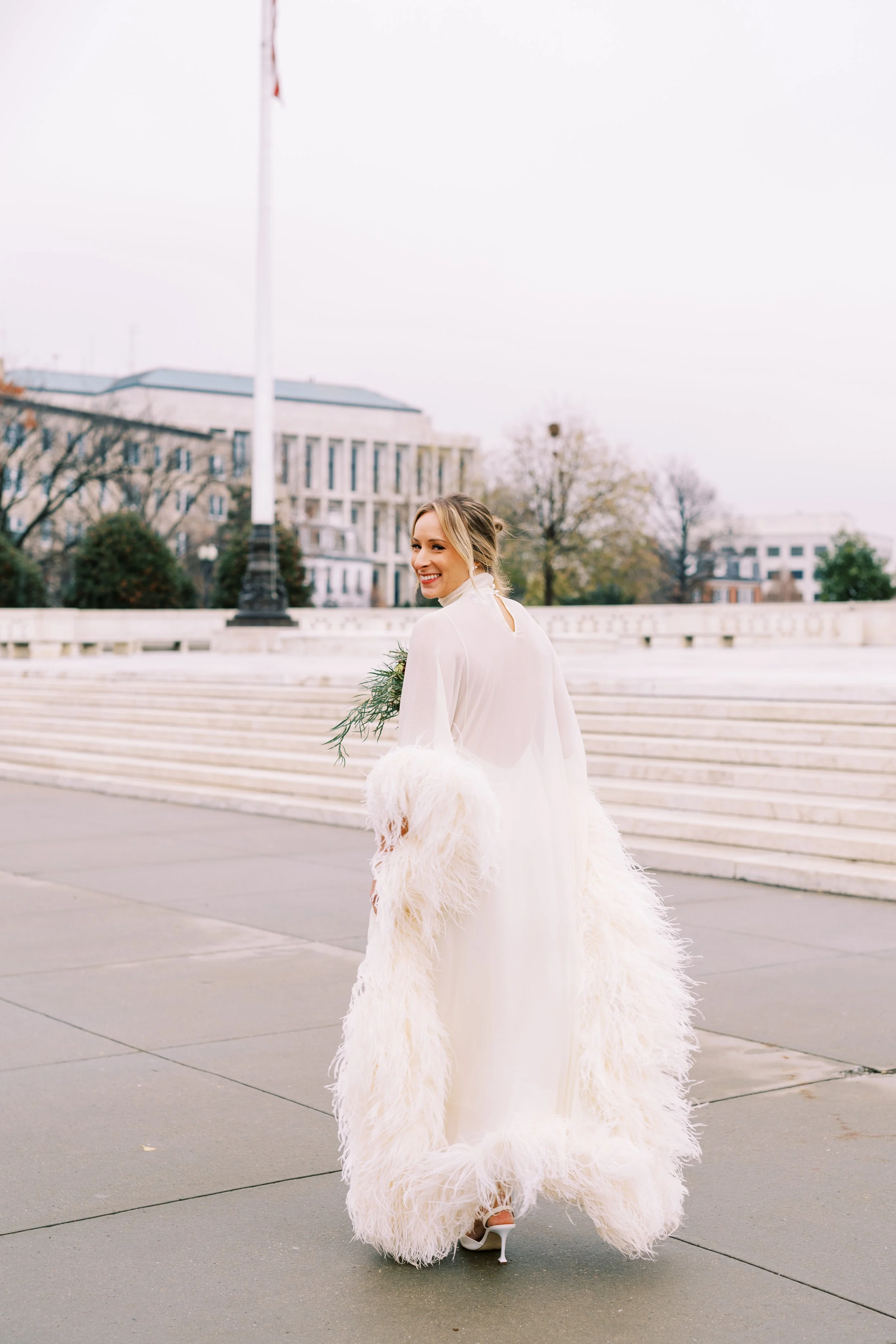 Bride walking solo across a plaza carrying her bouquet with Washington DC buildings in the background