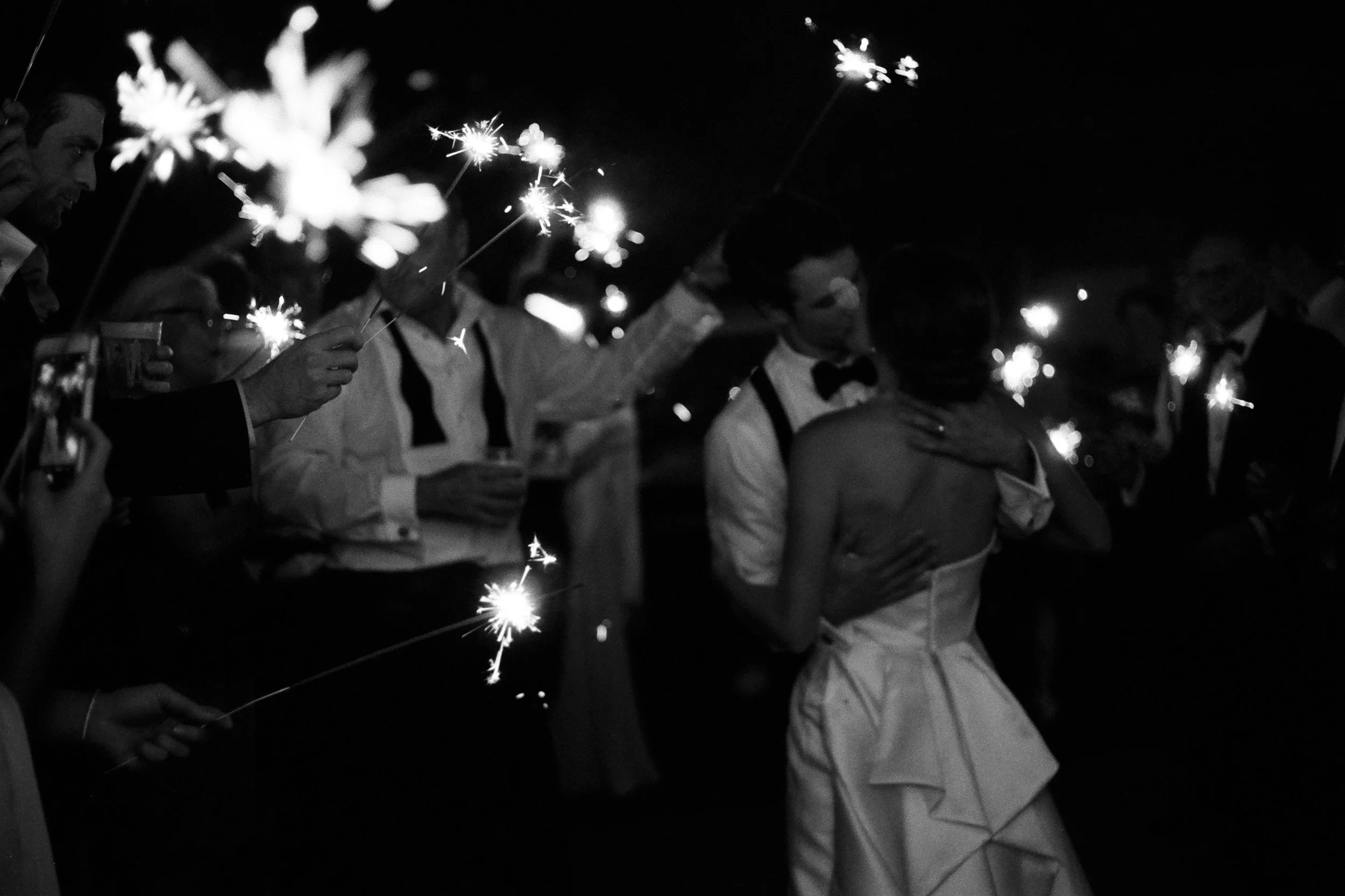 People holding sparklers at a nighttime wedding reception, with a couple dancing in the center.