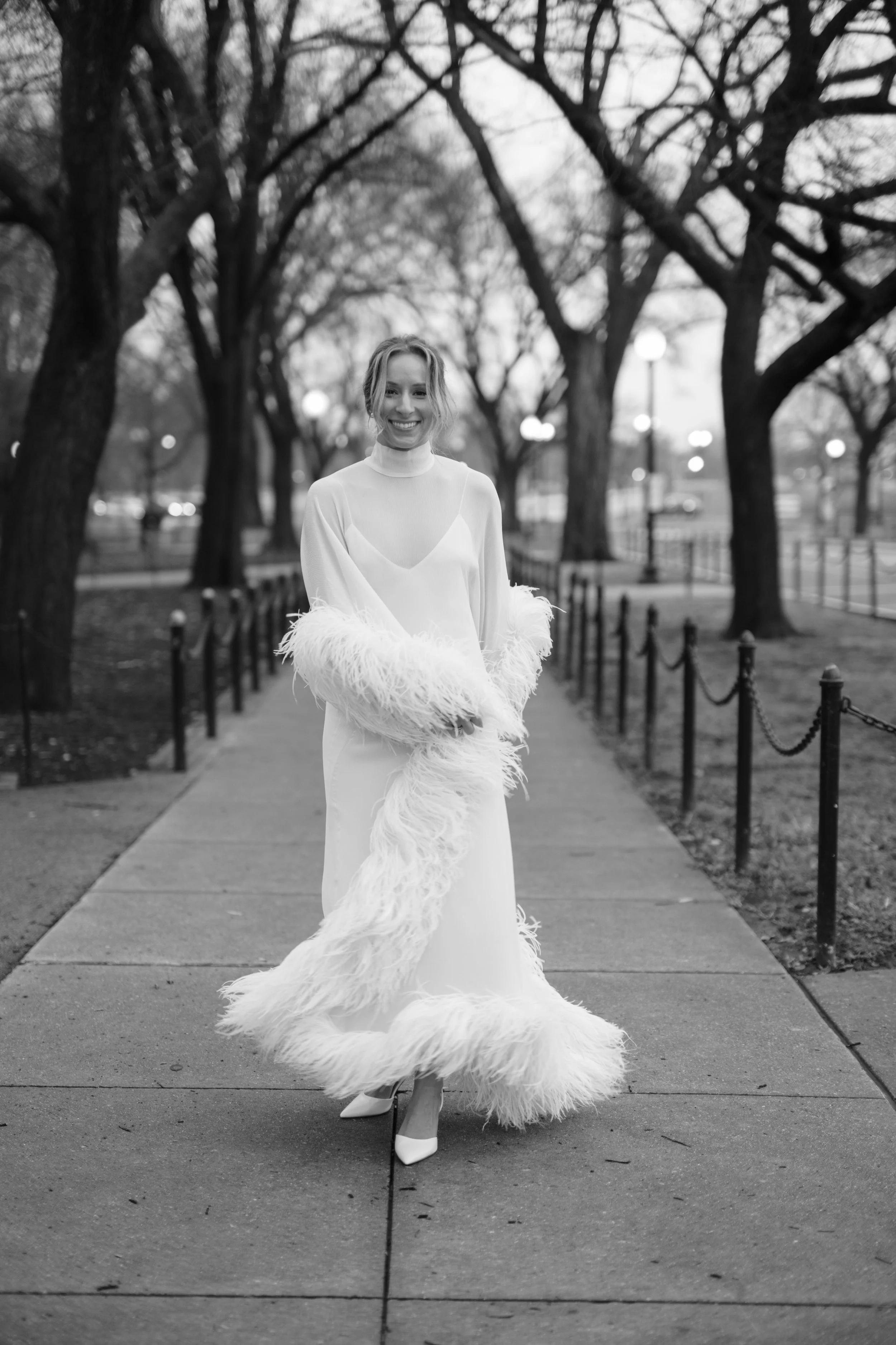 Black and white full-length photo of the bride walking down a tree-lined path