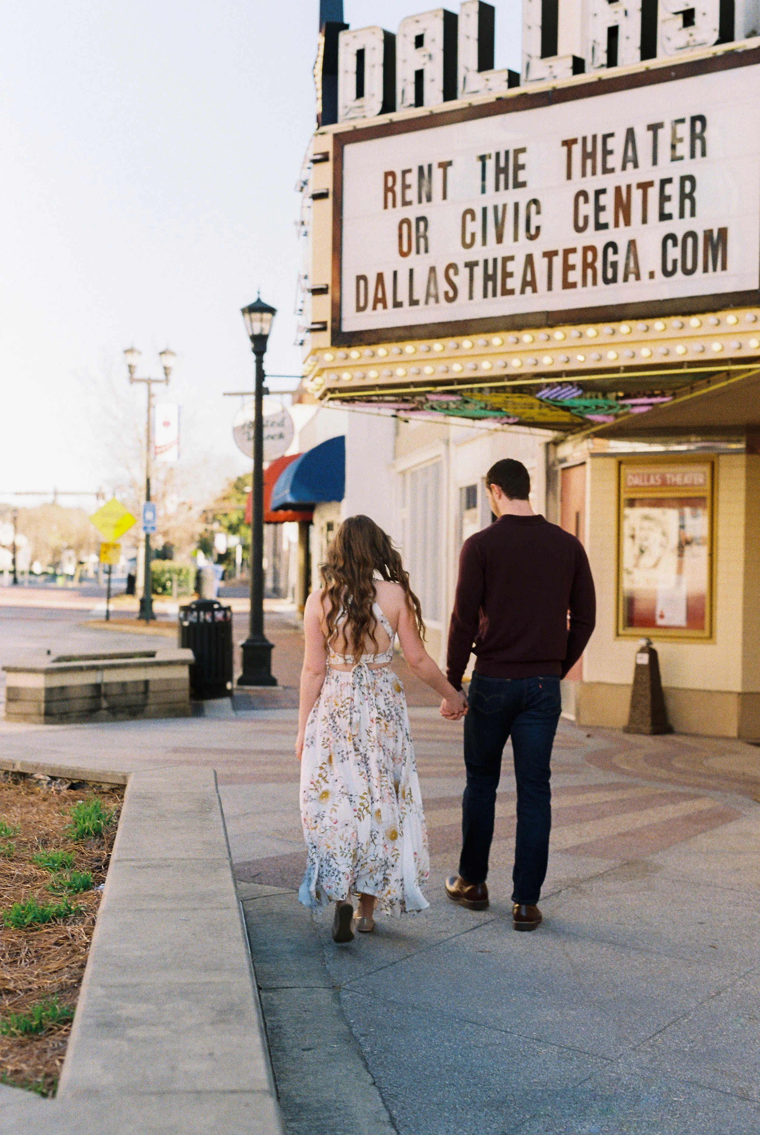 Conner and Maddie walk hand in hand away from the camera past the Dallas Theater marquee in downtown Dallas, Georgia.