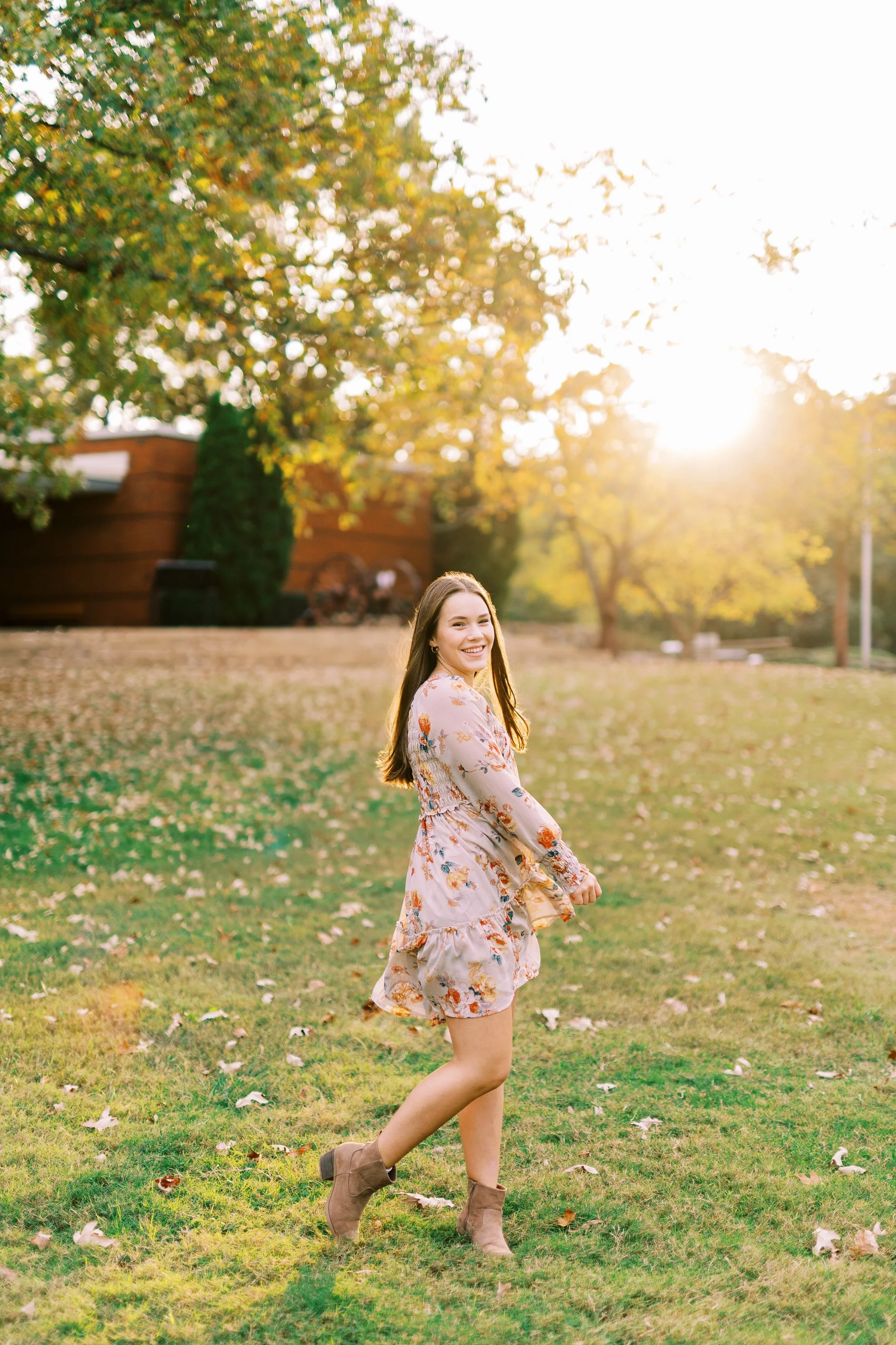 Senior portrait of Hannah walking across a sunlit lawn in a floral dress at Kennesaw Mountain Battlefield Park in Kennesaw, Georgia