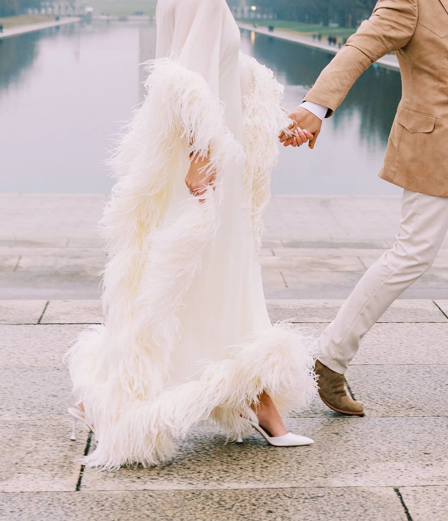 Bride and groom playfully running hand in hand along the reflecting pool